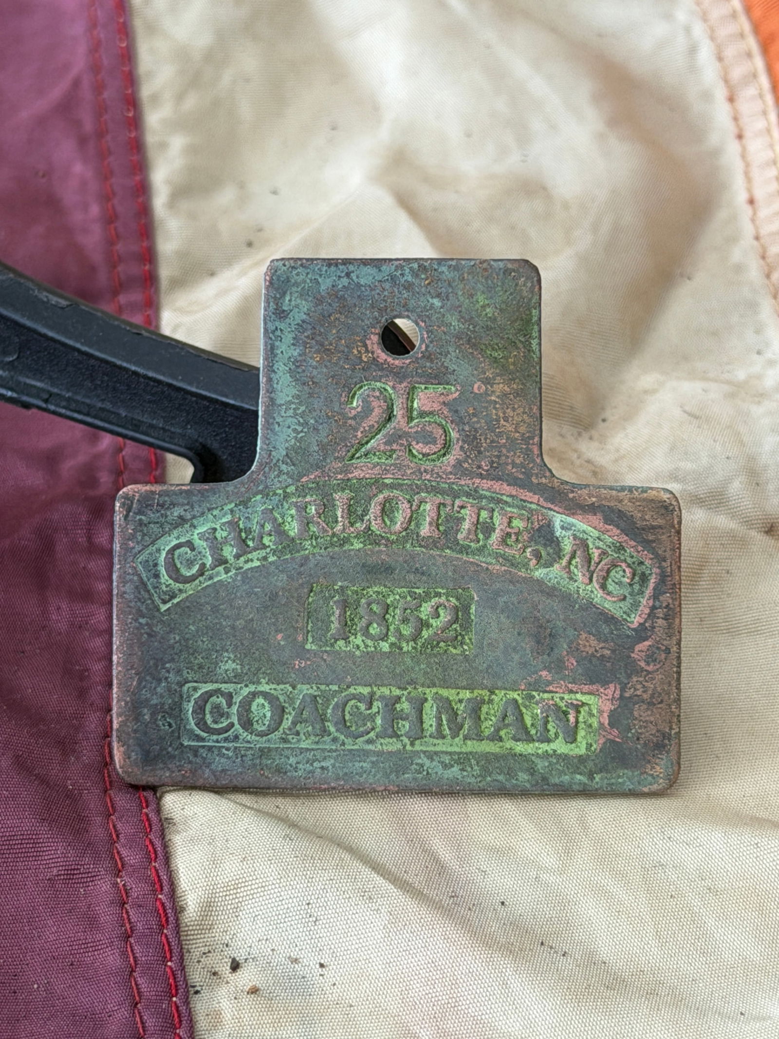License and Labor: 1852 Charlotte Coachman Slave Tag (No. 25): This copper-alloy slave hire tag, issued in 1852 by the city of Charlotte, North Carolina, bears the stamped designation “COACHMAN” and the identification number 25. Such tags were part of a m