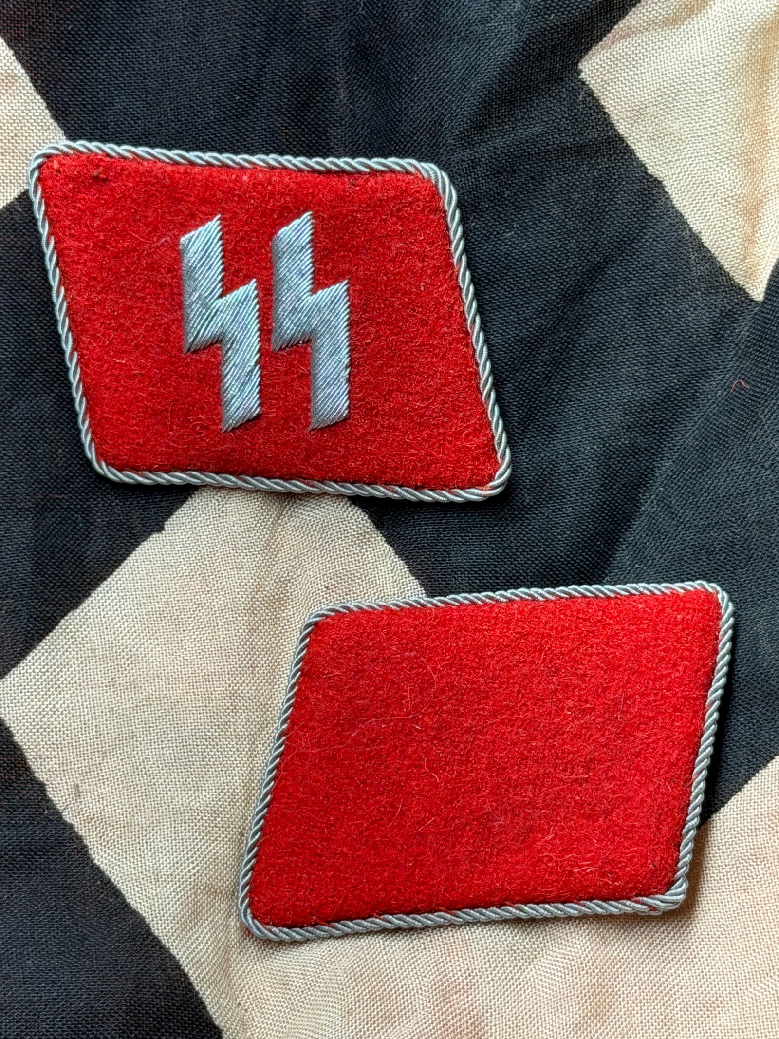 WW2 German Waffen-SS Collar Tabs (Pair): This matched pair of Waffen-SS collar tabs was worn on the uniform collar of enlisted personnel during the Second World War. The tabs feature the embroidered SS runes in silver-gray thread on red wool