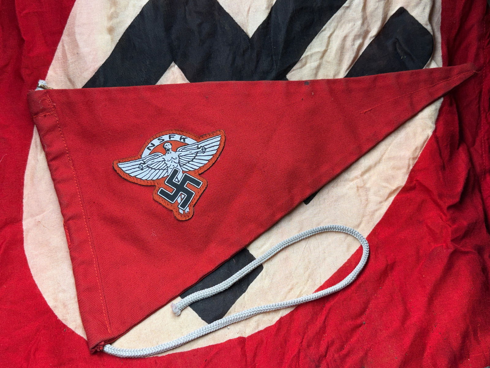 WW2 German NSFK Pennant (National Socialist Flying Corps), Germany, c. 1936–1939: This triangular red pennant bears the emblem of the NSFK (Nationalsozialistisches Fliegerkorps), a paramilitary organization of Nazi Germany tasked with promoting aviation skills and pre-military flig