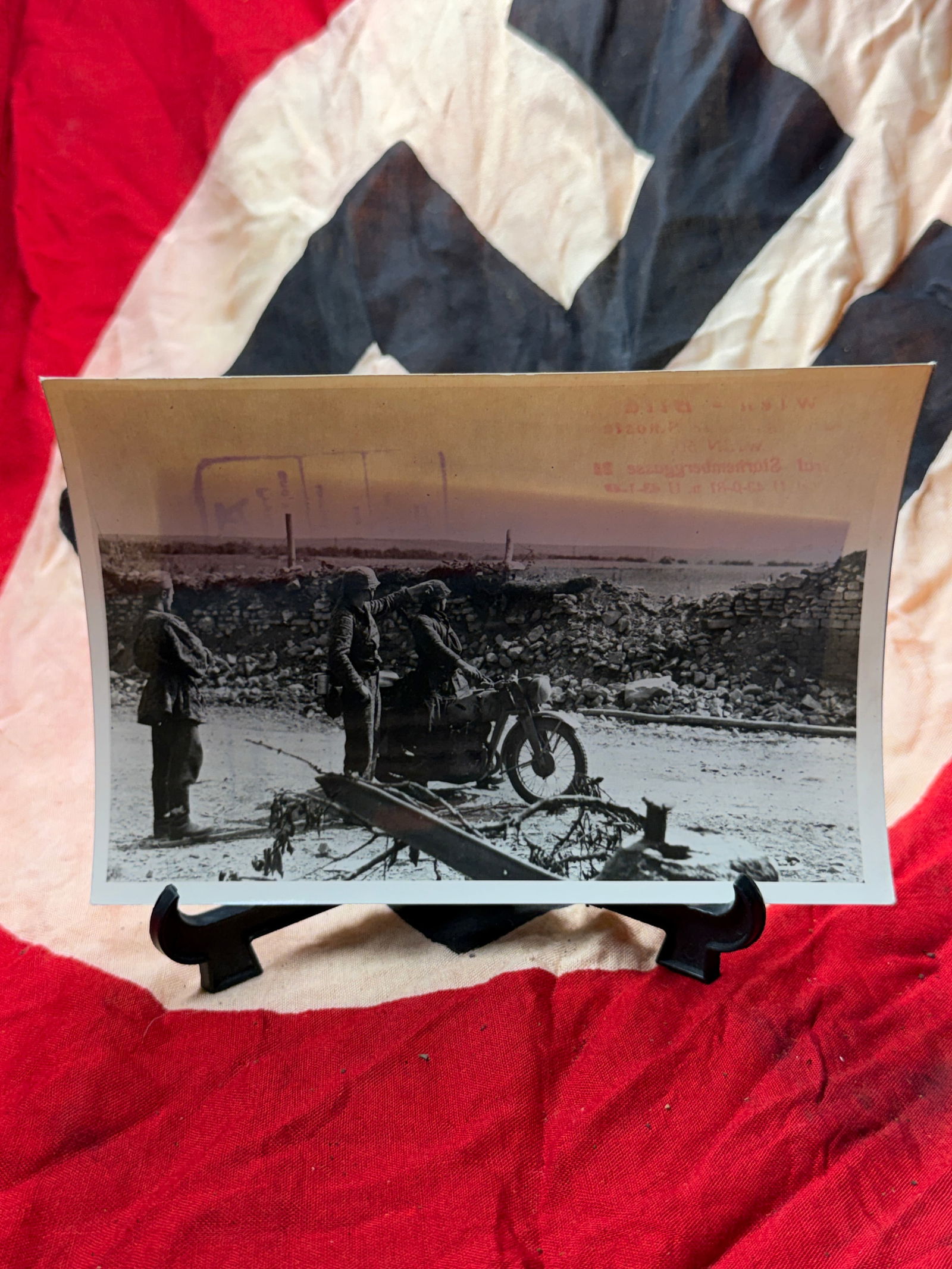WW2 German Motorcycle Dispatch at the Front With Certification: This period photograph captures a moment of military movement during the Second World War, showing uniformed German soldiers halted beside a motorcycle amid rubble and field fortifications. The image