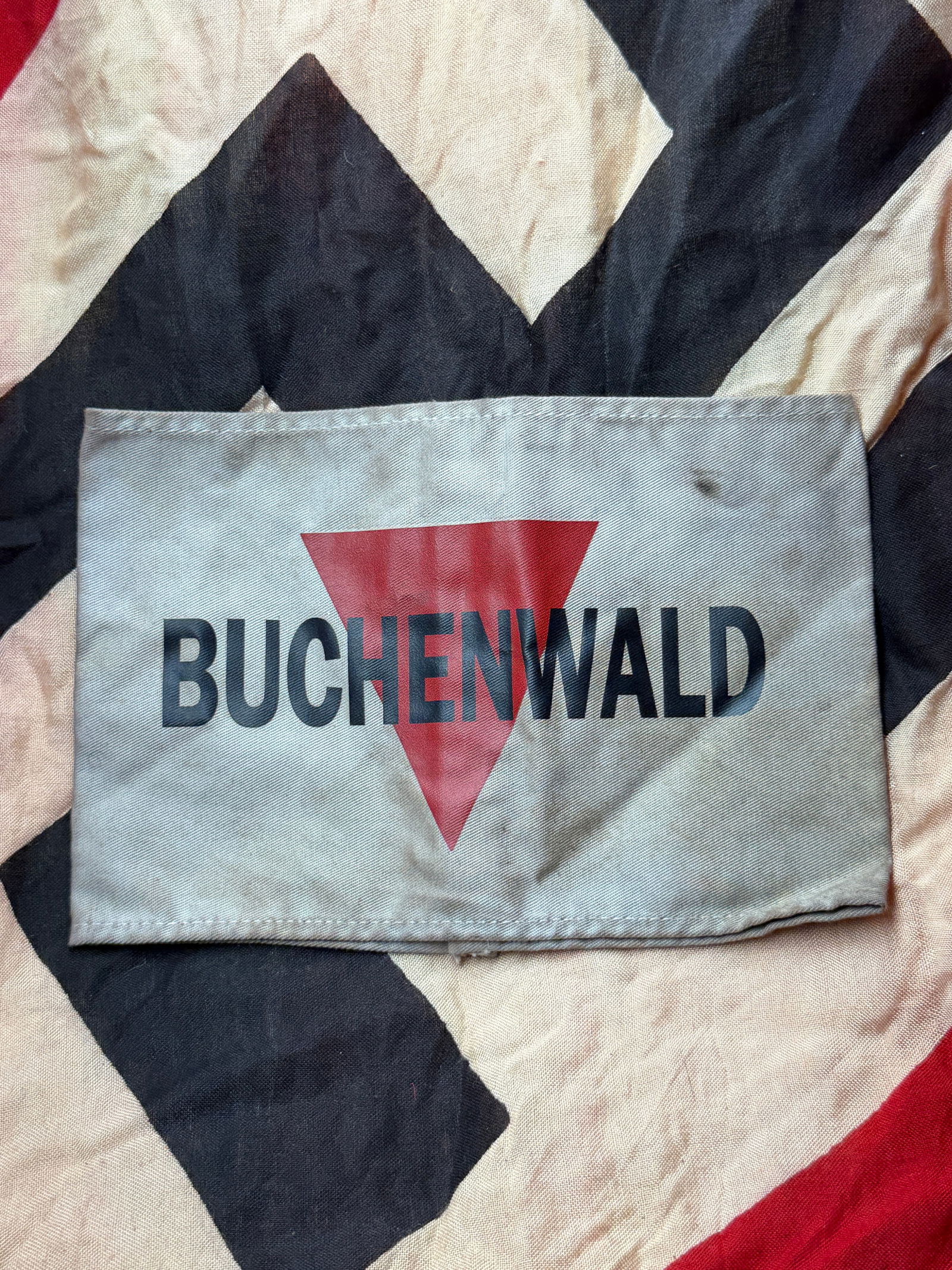 WW2 German Jewish Prisoner Identification Armband from Buchenwald Concentration Camp: This cloth armband, printed with the name “Buchenwald” over a red triangular symbol, was used within the Nazi concentration camp system during the Second World War. Such armbands functioned as