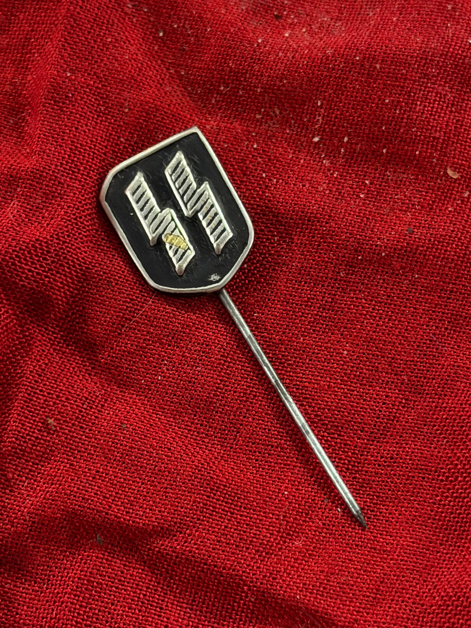 WW2 German Stick Pin with SS Runes: Small metal stick pin produced in Germany during the World War II period, featuring a shield-shaped emblem bearing the SS runic insignia in raised relief against a darkened field. The emblem is mounte
