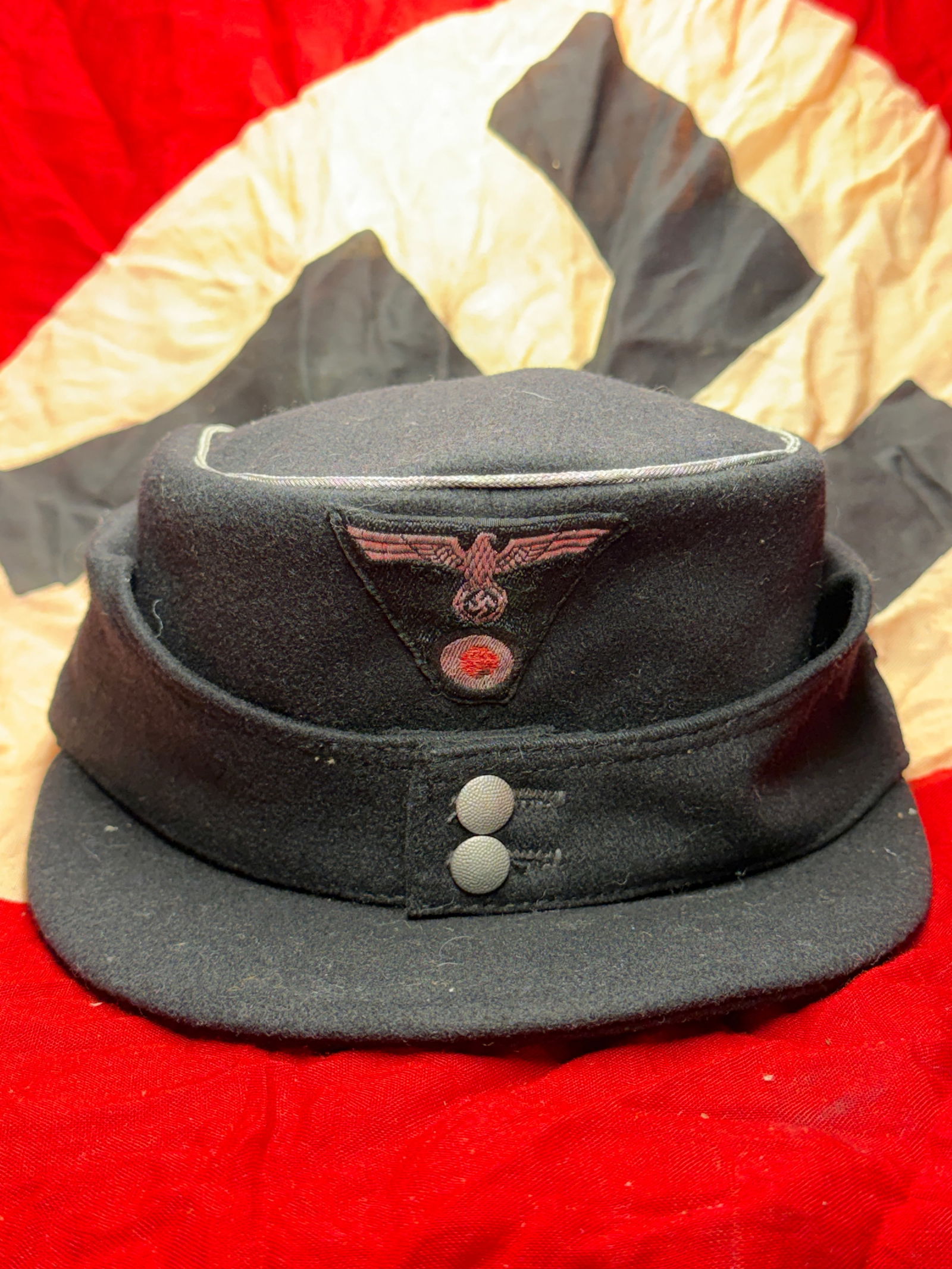 WW2 German Ordnungspolizei Field Cap (Einheitsfeldmütze): This wool field cap was worn by members of the German Ordnungspolizei (Order Police) during the Second World War. Constructed in dark field-grey wool, the cap features silver-grey piping along the cro