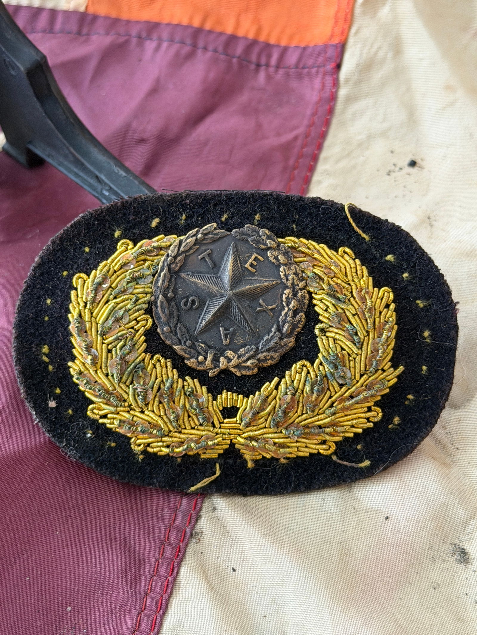 Civil War Texas State Officer’s Hat Badge (Lone Star Wreath Insignia): This embroidered hat badge features the Texas Lone Star encircled by a laurel wreath and mounted on a black wool backing. At the center is a metal five-pointed star bearing the letters T E X A S, a lo