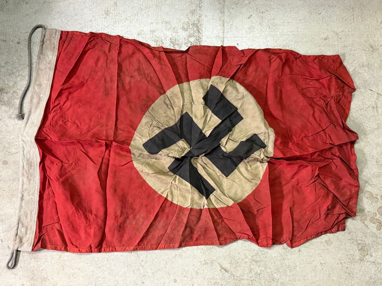 WW2 German National Socialist Flag (Hoist-Type): Flag bears the emblem of the National Socialist German Workers’ Party (NSDAP): a black swastika within a white roundel on a red field. The flag is constructed of lightweight red fabric with a reinfo