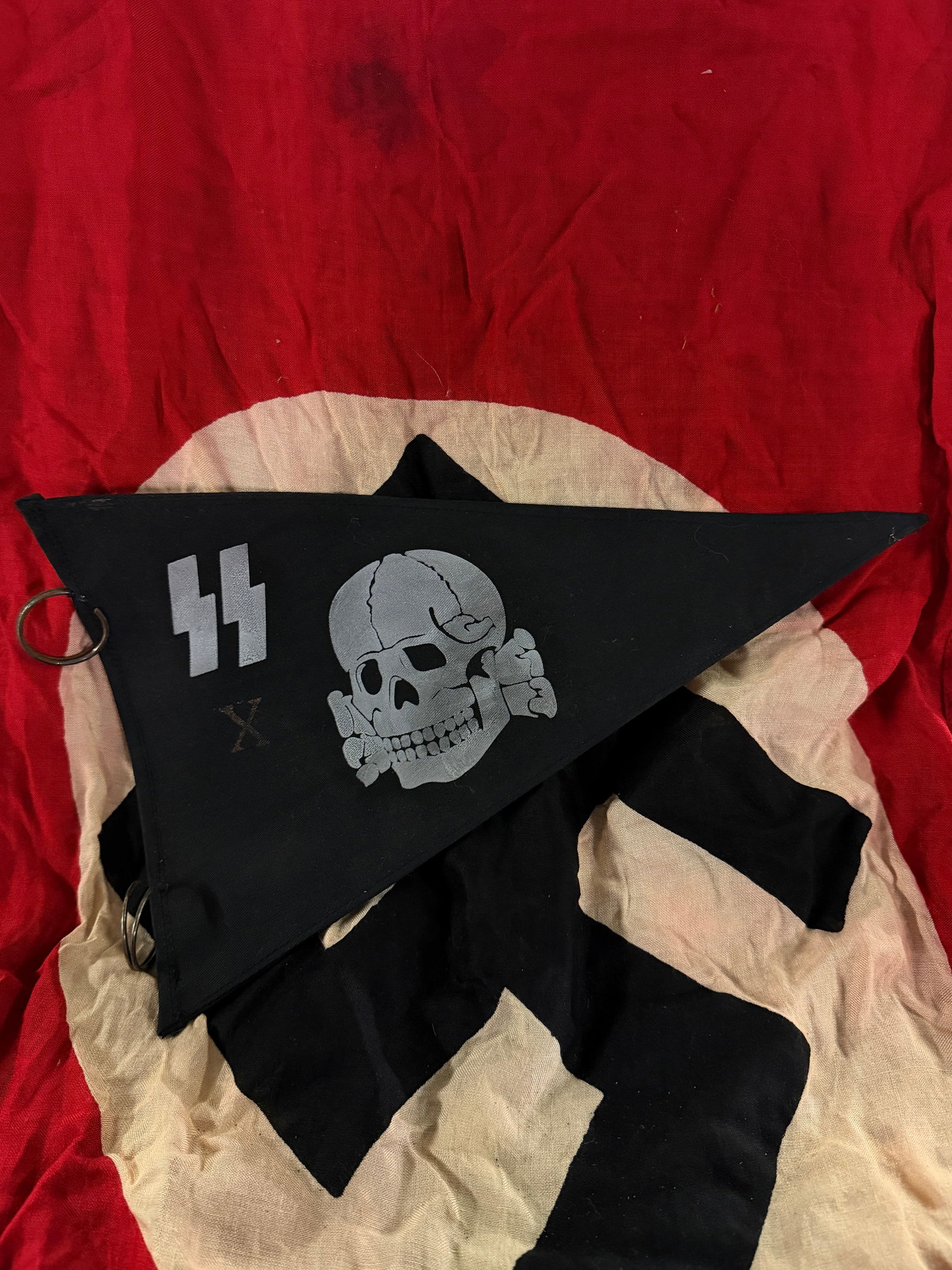 WW2 German SS Totenkopf Pennant (Death’s Head Insignia): This triangular black cloth pennant features the Totenkopf (death’s head) emblem associated with the German SS (Schutzstaffel) during the World War II period. The design includes a stylized skull wi