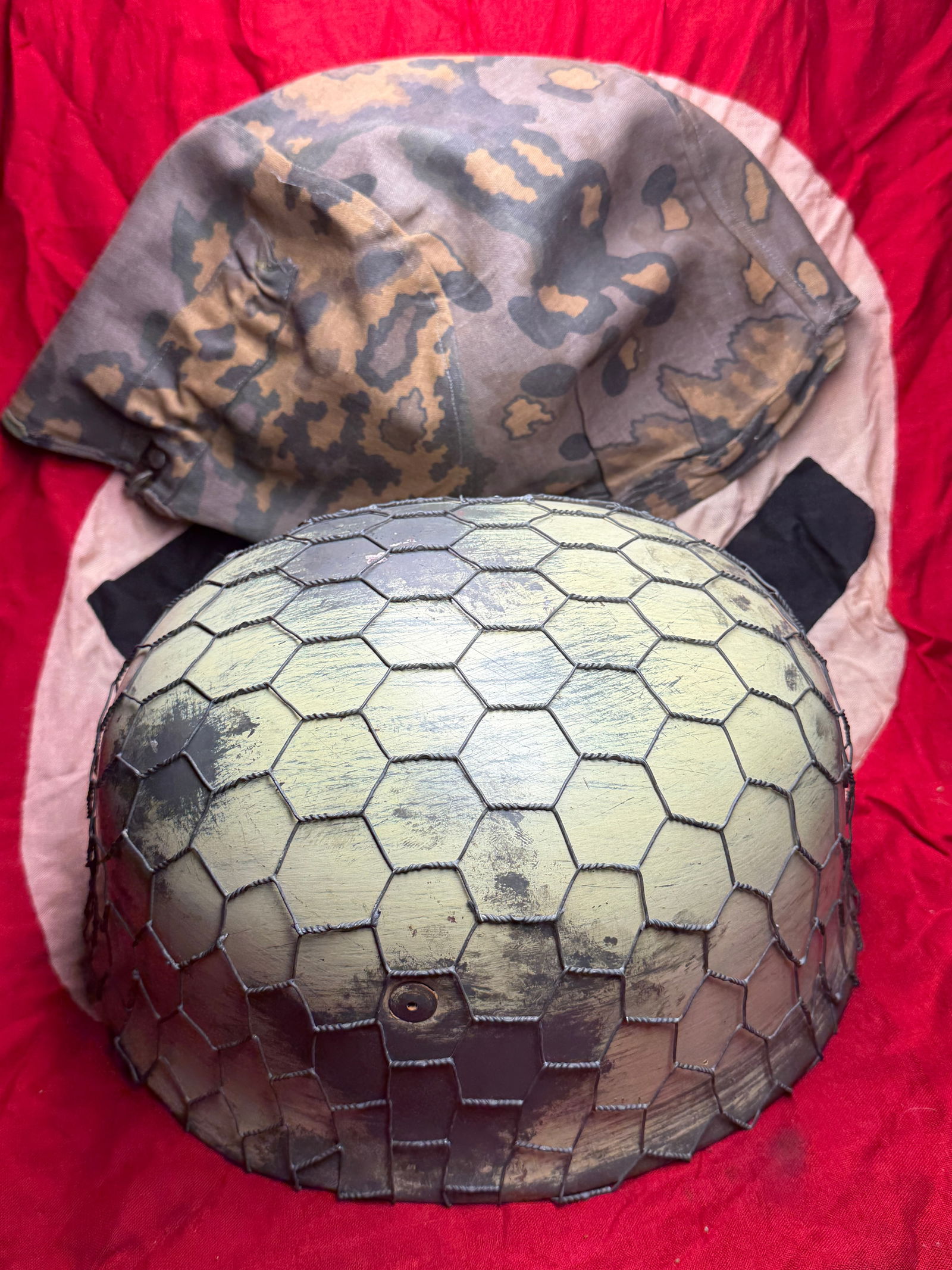 WW2 German Camouflaged German Steel Combat Helmet (Stahlhelm M35/M40 Pattern): This artifact consists of a German steel combat helmet (Stahlhelm), fitted with a period camouflage helmet cover and protective wire netting. The helmet is of the M35/M40 pattern, widely issued to Ger