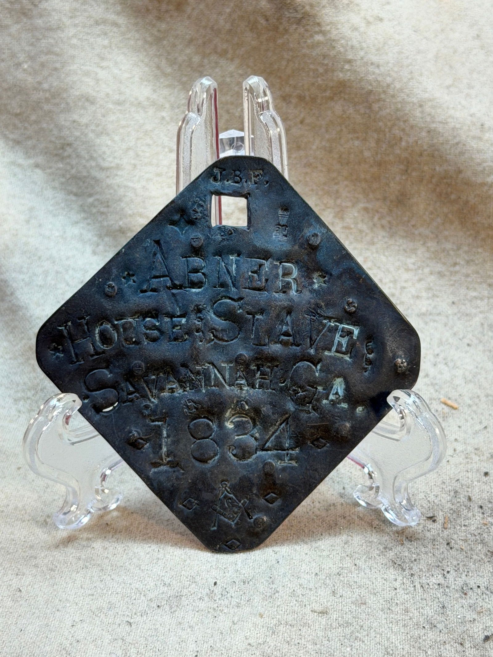 Identification Badge of an Enslaved Person: Abner Savannah, Georgia, 1834: This metal identification badge is inscribed “Abner / House Slave / Savannah, GA / 1834”, identifying an enslaved individual named Abner living in Savannah, Georgia, in the early 19th century.