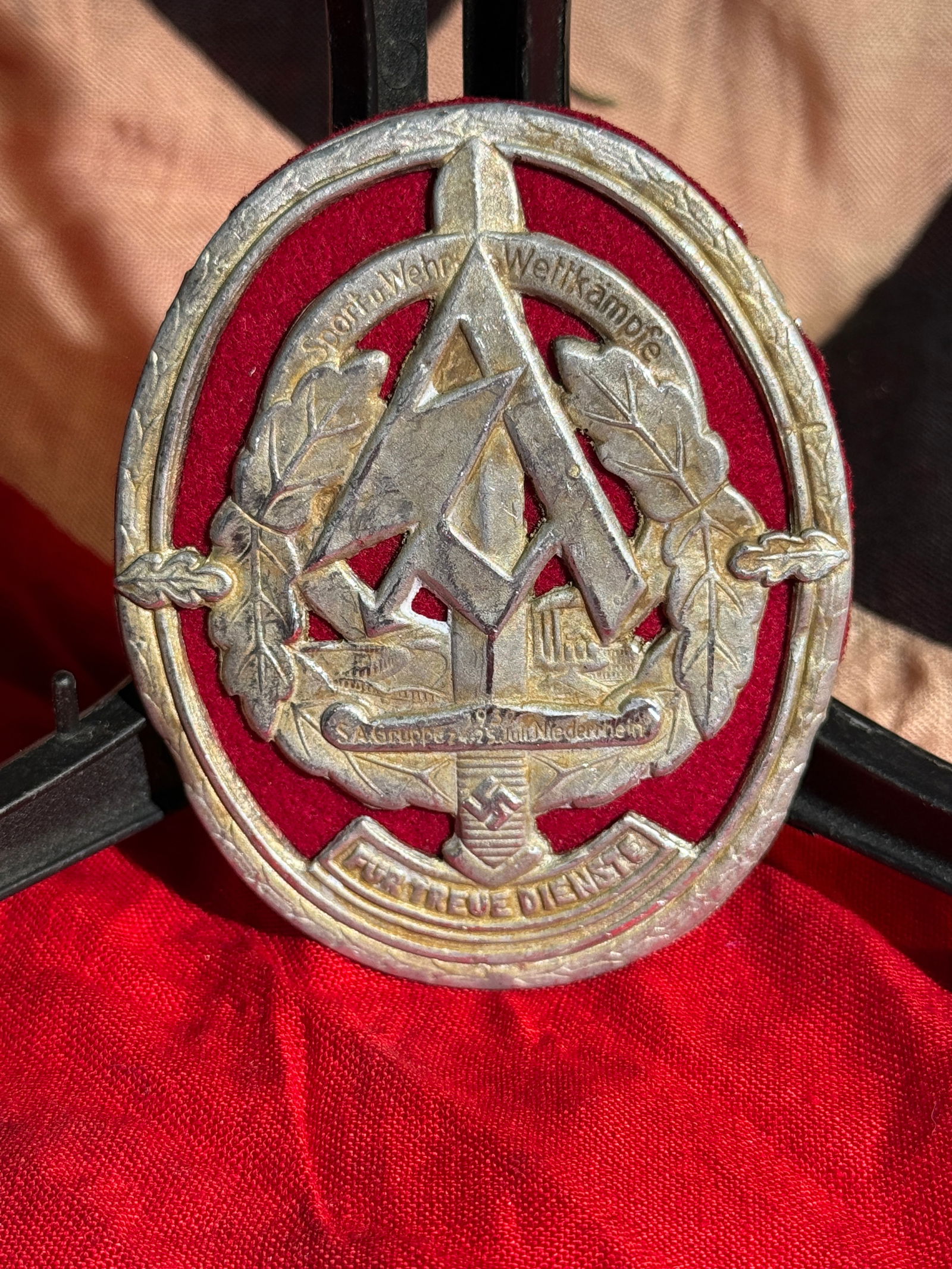 WW2 German SA Group Lower Rhine Sport and Defense Competition Badge, 1938 - RZM Maker Marked: RZM Maker Marked German SA Sport und Wehr Wettkämpfe (Sport and Defense Competition) badge mounted on a red cloth backing. The design features the SA emblem within an oak-leaf wreath, with inscriptio