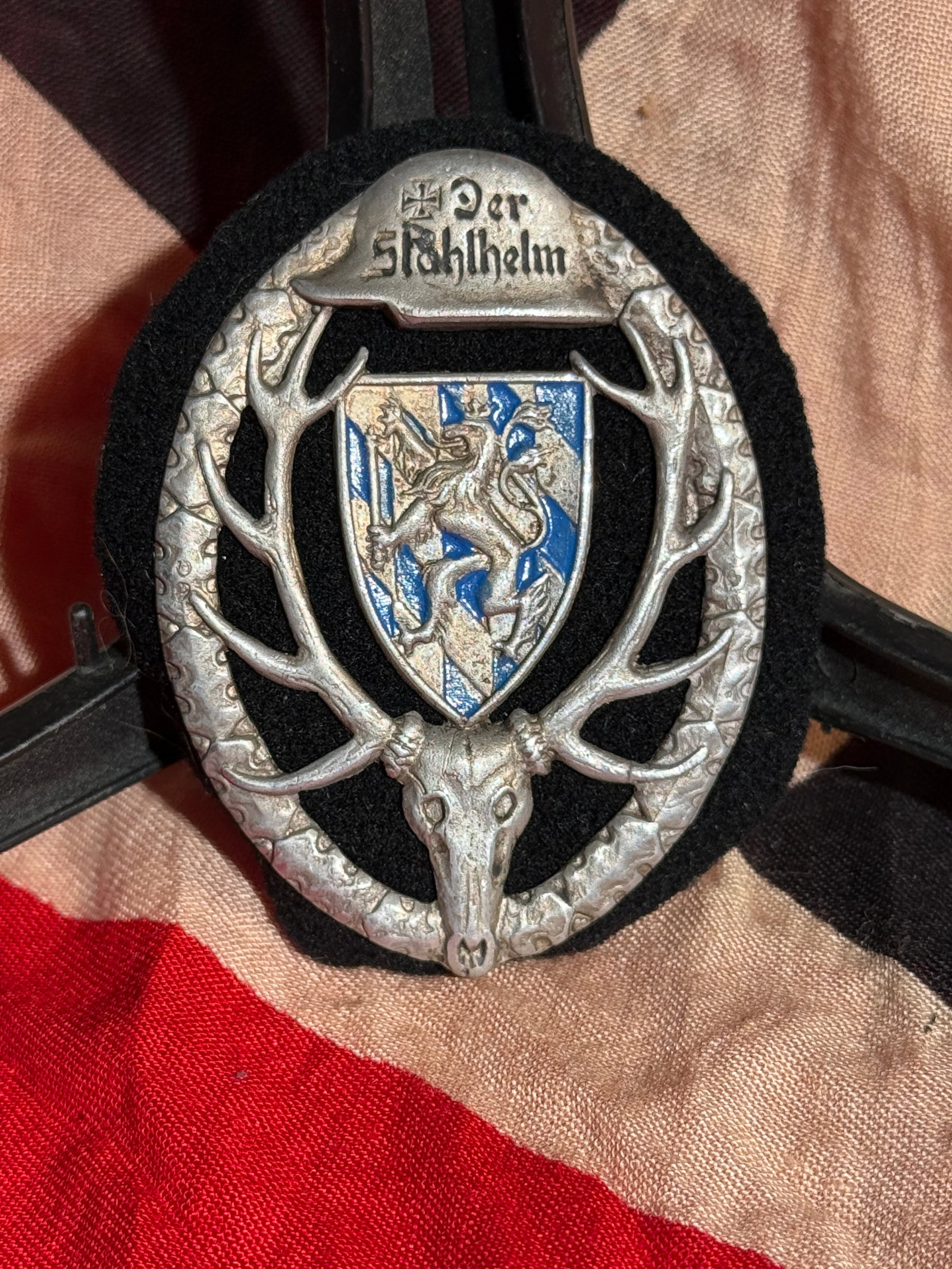 WW2 German Hunting Association Badge with Bavarian Coat of Arms and “Der Stahlhelm?? Helmet -: Maker Marked German hunting association (Jäger) badge featuring a stag skull and antlers surrounding a Bavarian coat of arms with lion and blue-white lozenges. Above the shield is a helmet bearing th