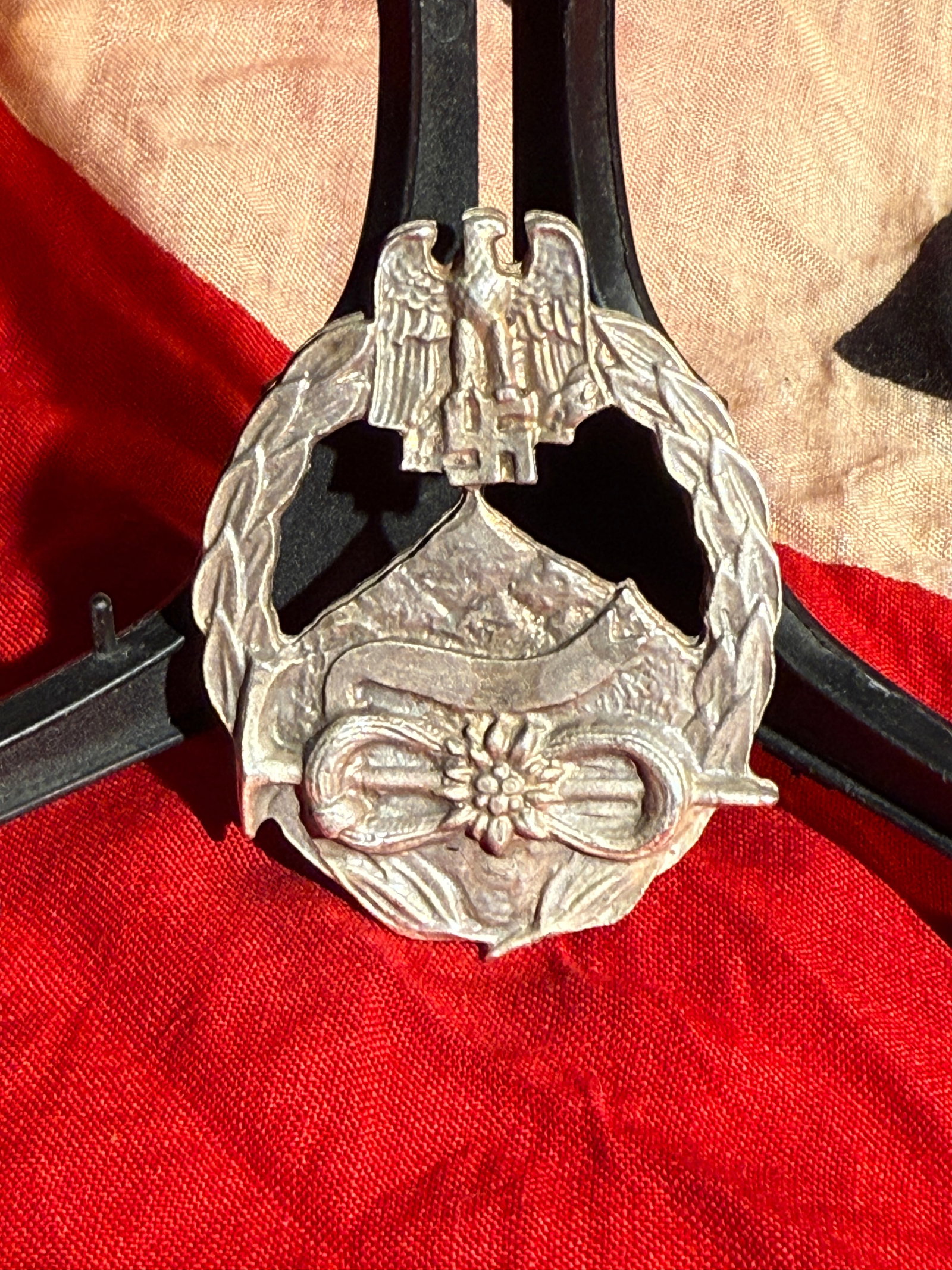German Gebirgsjäger Cap Badge with Edelweiss (World War II Era) Maker Marked Berlin: Maker marked World War II–era German Gebirgsjäger (Mountain Troops) cap badge featuring a stylized edelweiss flower set on a mountain landscape within a wreath, surmounted by a spread-wing eagle. T