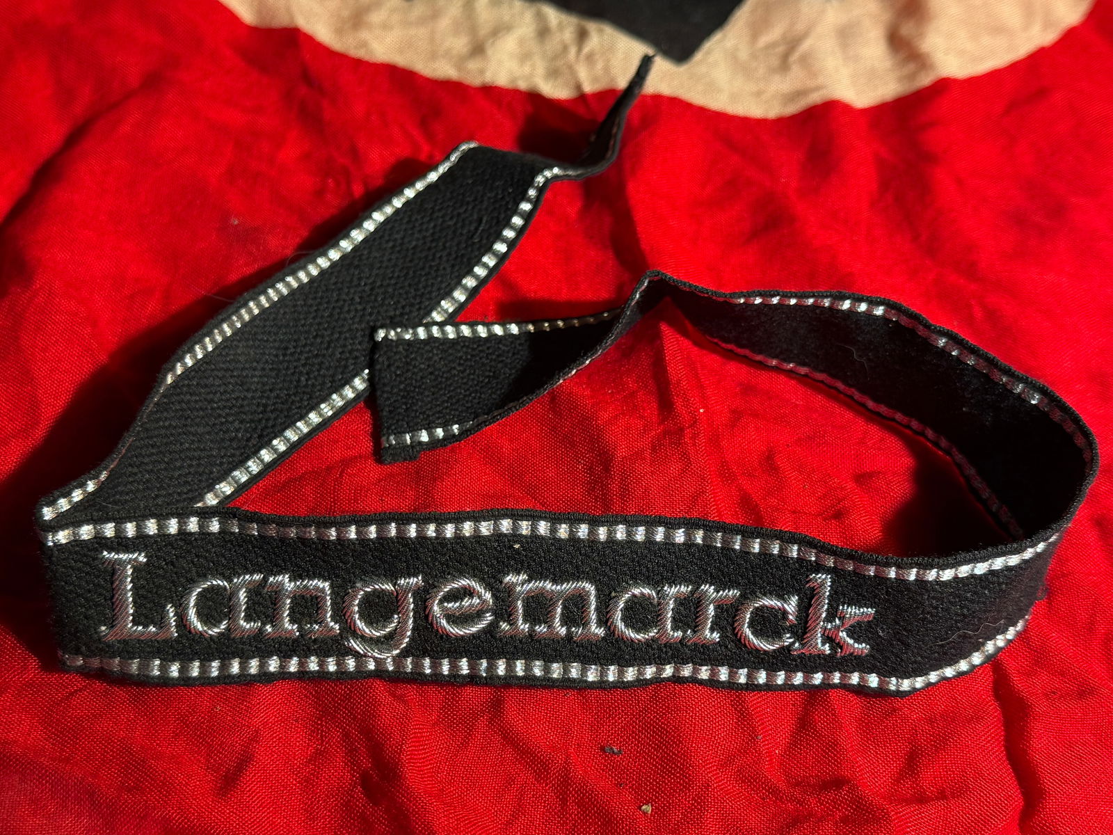 WWII German Luftwaffe “Langemarck?? Cuff Title (Ärmelband): Black woven Luftwaffe cuff title embroidered “Langemarck” in silver thread, worn on the sleeve of uniforms by members of Luftwaffe units associated with the Langemarck tradition. The title com