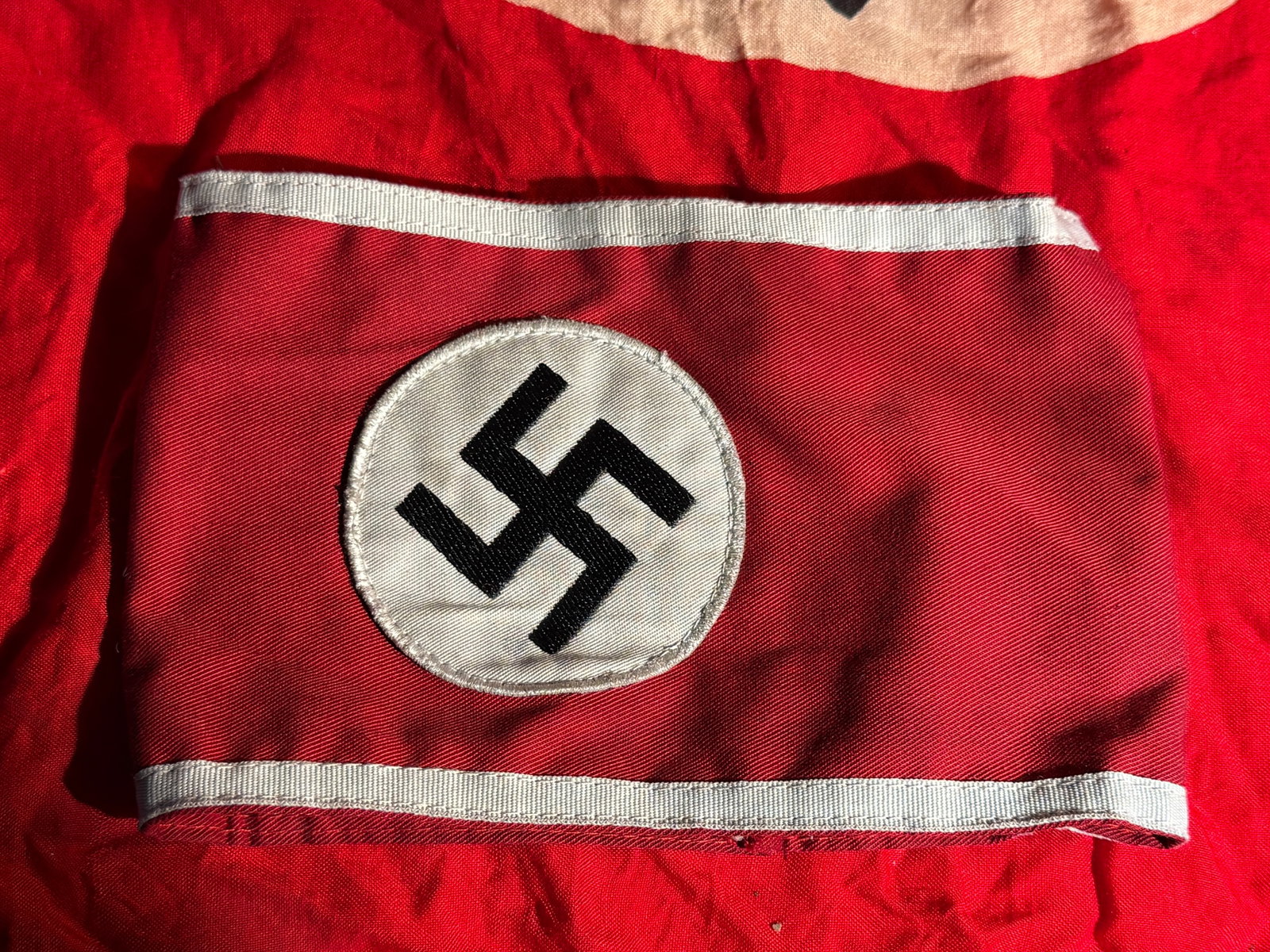 WW2 German NSDAP Armband with RZM Tag, Nazi Germany, c. 1933–1945: Red cloth National Socialist German Workers’ Party (NSDAP) armband featuring a white roundel with a black swastika at the center and white edge borders. Armbands such as this were worn on the upper 