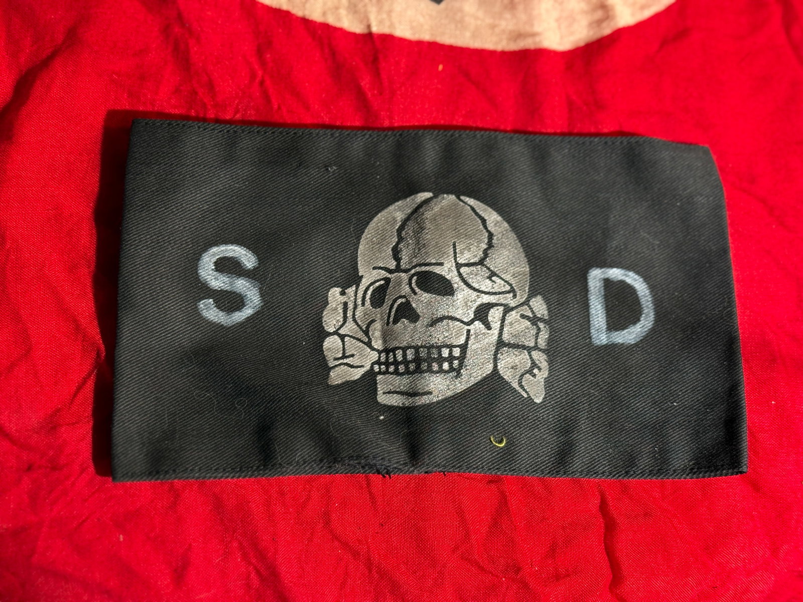 WW2 German SS SD Totenkopf Guard Armband (Skull Armband) With RZM Paper Tag: Black cloth SS armband featuring the Totenkopf (death’s head) skull emblem flanked by the letters “S” and “D.” The skull symbol was associated with SS-Totenkopf units, which were res