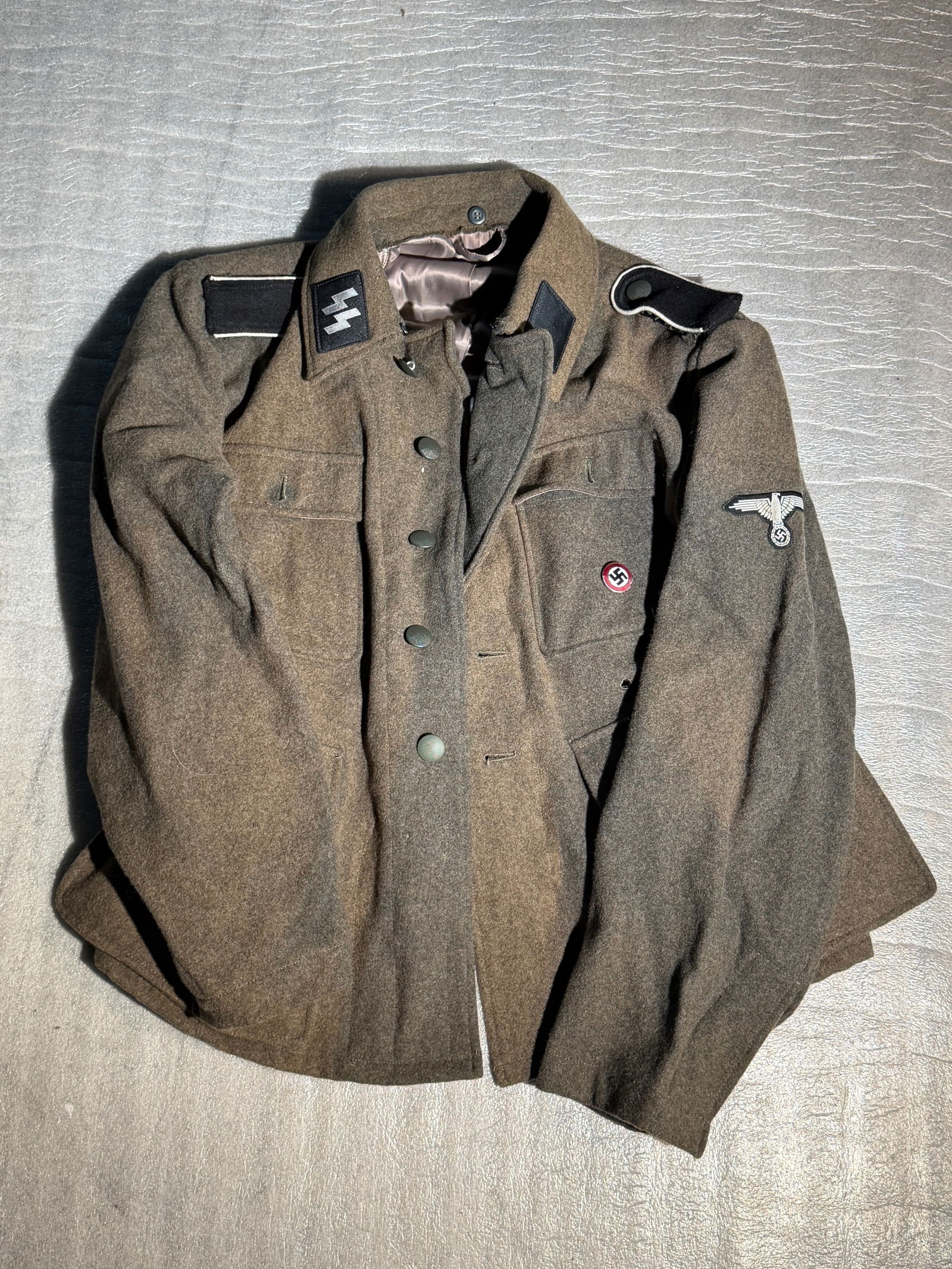 WW2 German Waffen-SS Field Tunic (Service Uniform), Nazi Germany - Maker Marked: This wool field tunic is associated with the Waffen-SS, the armed combat branch of the Schutzstaffel (SS) in Nazi Germany during the Second World War (1939–1945). The brown-grey uniform jacket featu