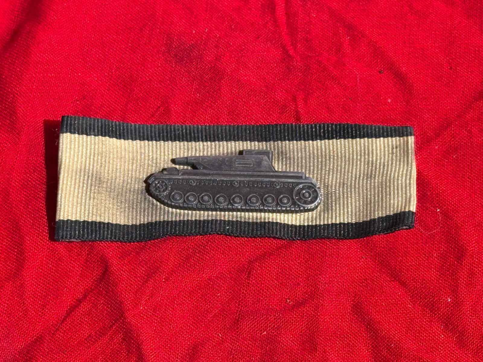 German Panzer Assault Ribbon Bar with Miniature Tank Device, Nazi Germany, World War II Era (c.: Cloth ribbon bar representing the Panzer Assault Badge (Panzerkampfabzeichen), worn on the service tunic of German armored troops during the Second World War. The bar consists of a cream-colored ribbo