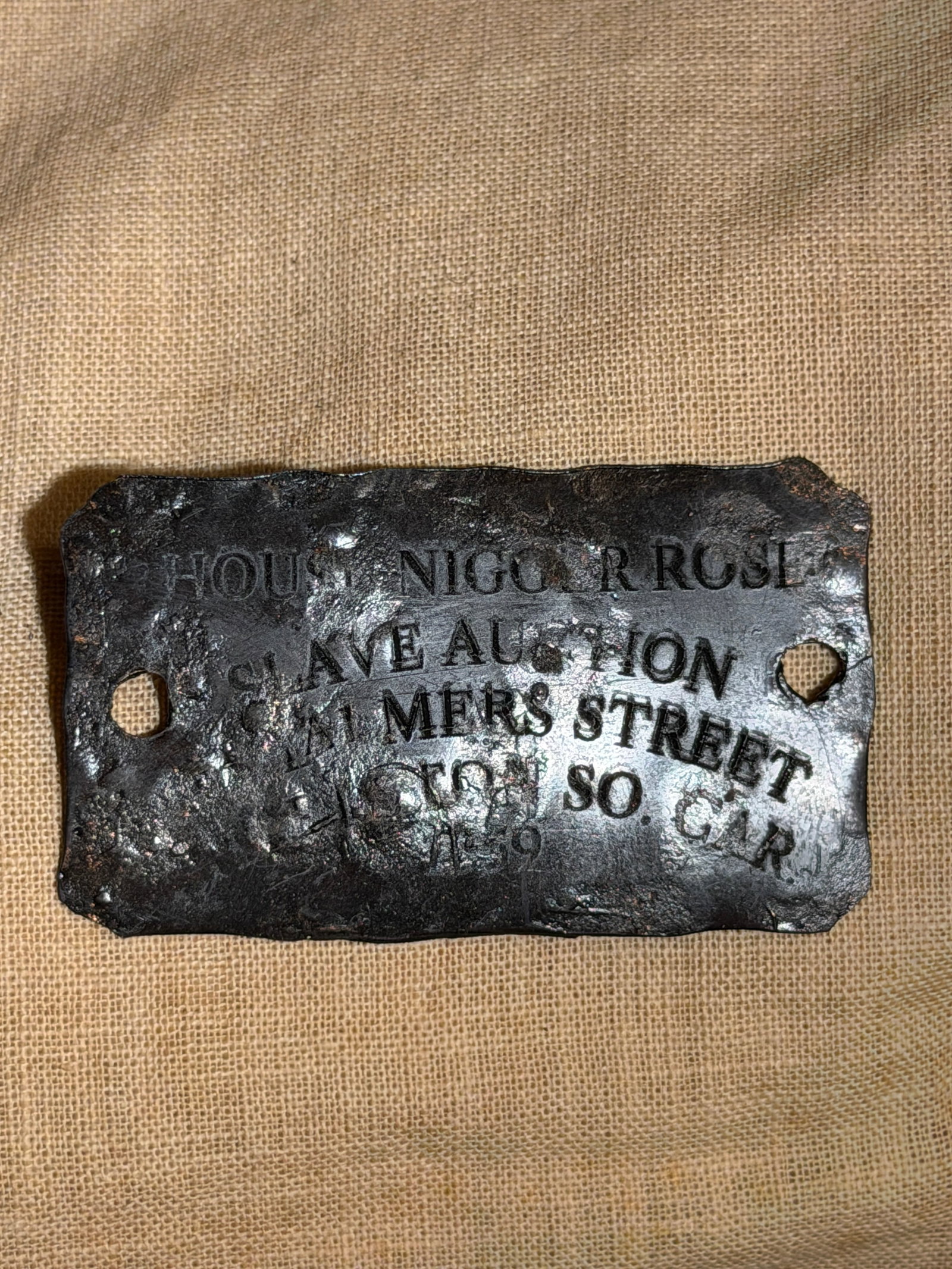 Rare Slave Tag Engraved Metal Plate Referencing Enslaved Labor, Dated 1859: Rectangular engraved metal plate bearing partially legible text referencing enslaved individuals and an auction, dated 1859. The plate includes two mounting holes, suggesting it was affixed to a surfa