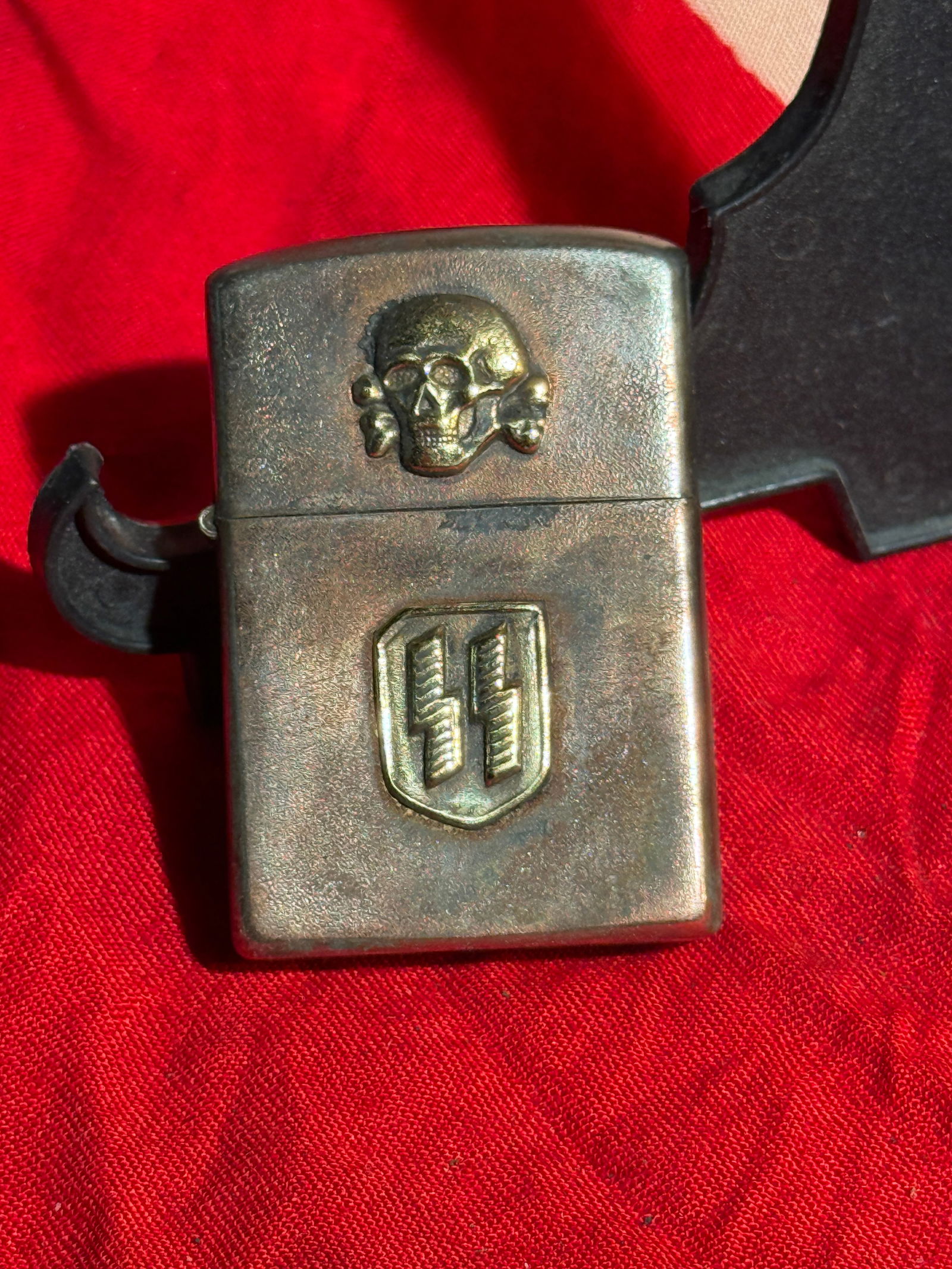 German WWII SS Totenkopf Emblem Lighter - Field Used By RZM: Metal petrol lighter featuring an SS Totenkopf (skull and crossbones) emblem on the lid and an SS rune shield insignia on the body. The lighter is constructed with a hinged lid and internal flint-whee