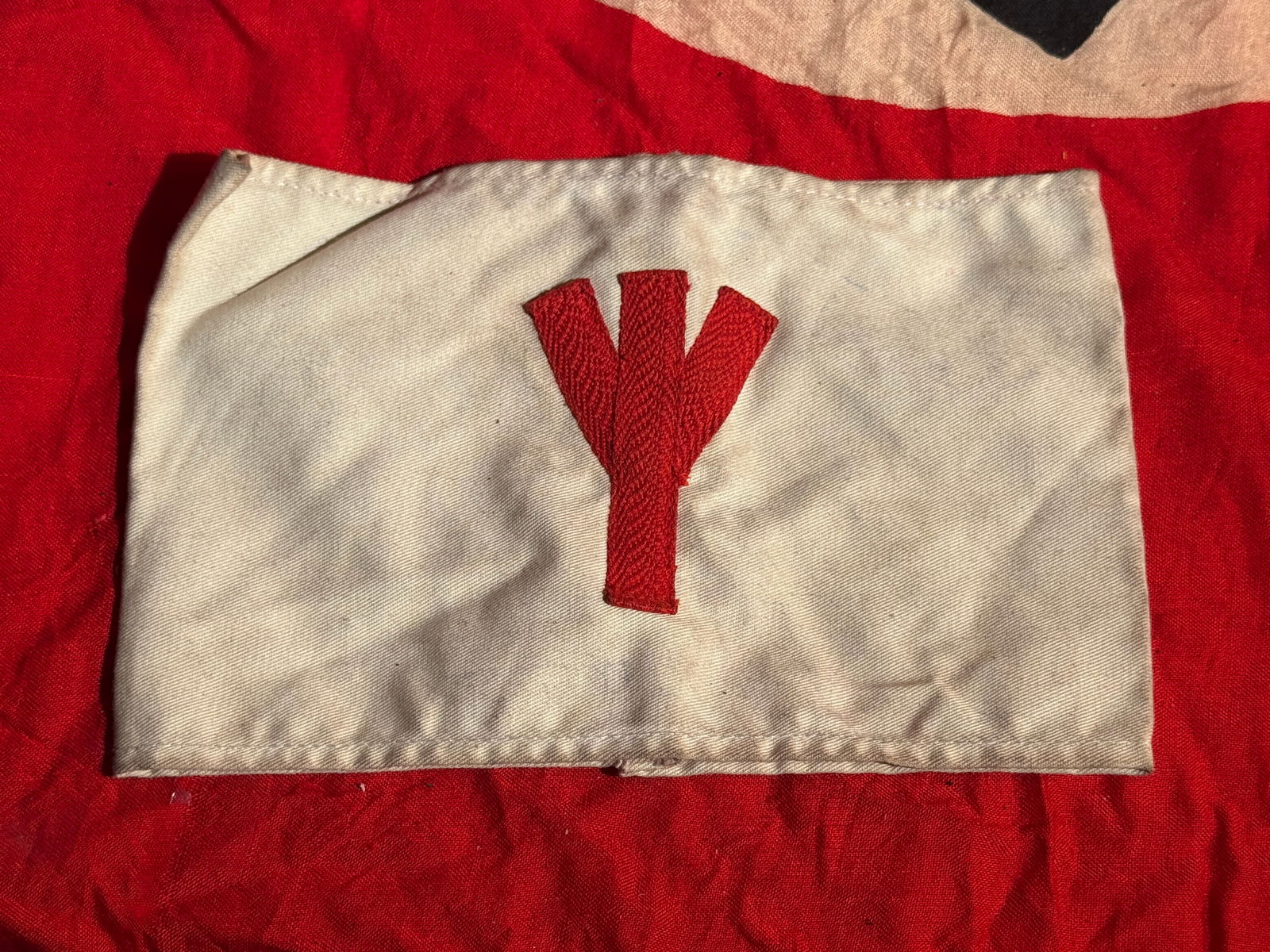 German WWII Volkssturm Armband: White cloth armband bearing a red “Y”-shaped insignia, associated with units of the Volkssturm, the German national militia formed in the final months of the Second World War (1944–1945). Ar