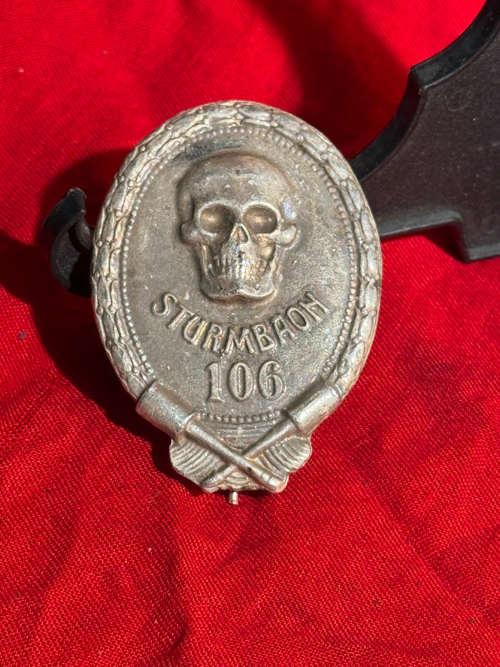 German Sturmabteilung (SA) “Sturmbann 106?? Badge: Oval metal badge featuring a skull (Totenkopf) above the inscription “STURMBANN 106,” framed by a wreath and crossed weapons at the base. Such badges were associated with units of the Sturmabt