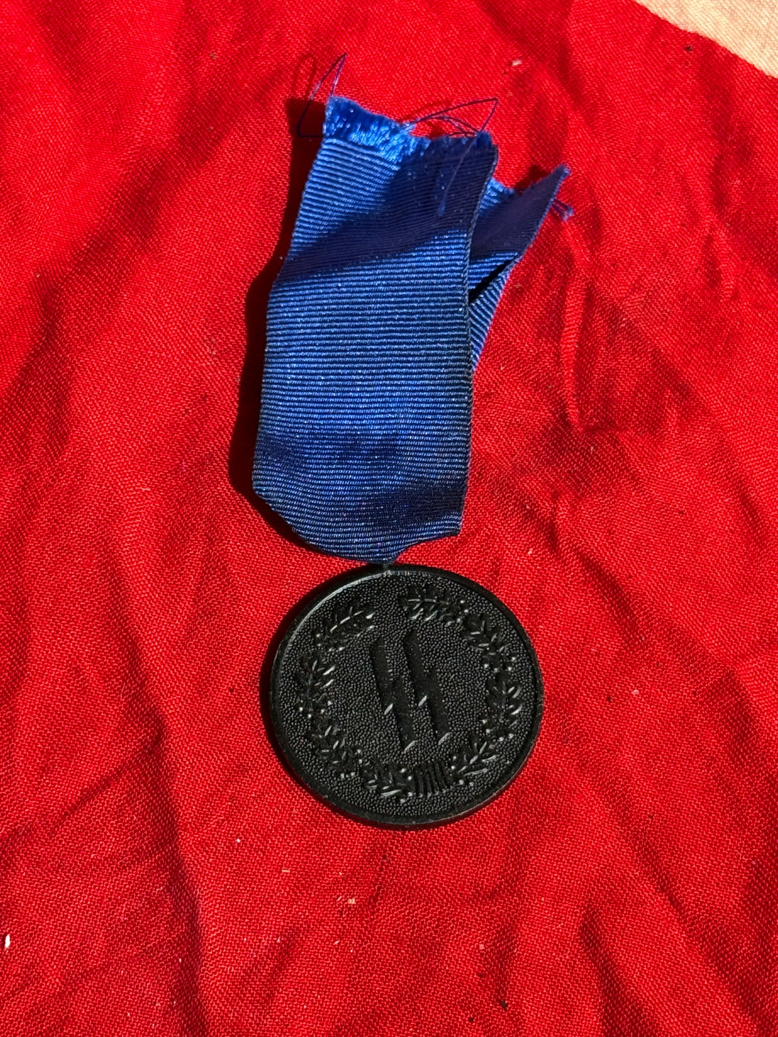 WW2 German SS Long Service Medal, 4 Years (SS-Dienstauszeichnung), Third Reich Germany: Round blackened medal suspended from a dark blue ribbon, awarded for four years of loyal service in the Schutzstaffel (SS) during the Third Reich period. The obverse features the SS runes surrounded b