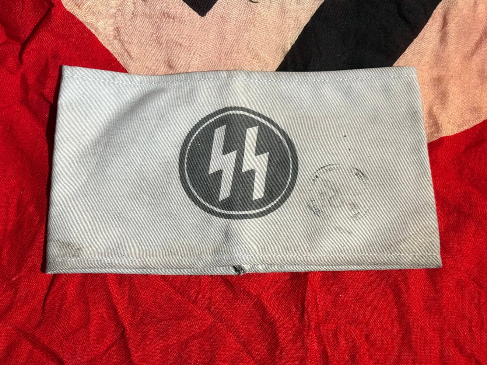WW2 German Waffen SS Organizational Armband with RZM Tag: Light gray cloth armband featuring the black SS runes (Sig runes) within a circular emblem, worn by members of the Schutzstaffel (SS) of Nazi Germany. The armband retains its original Reichszeugmeiste