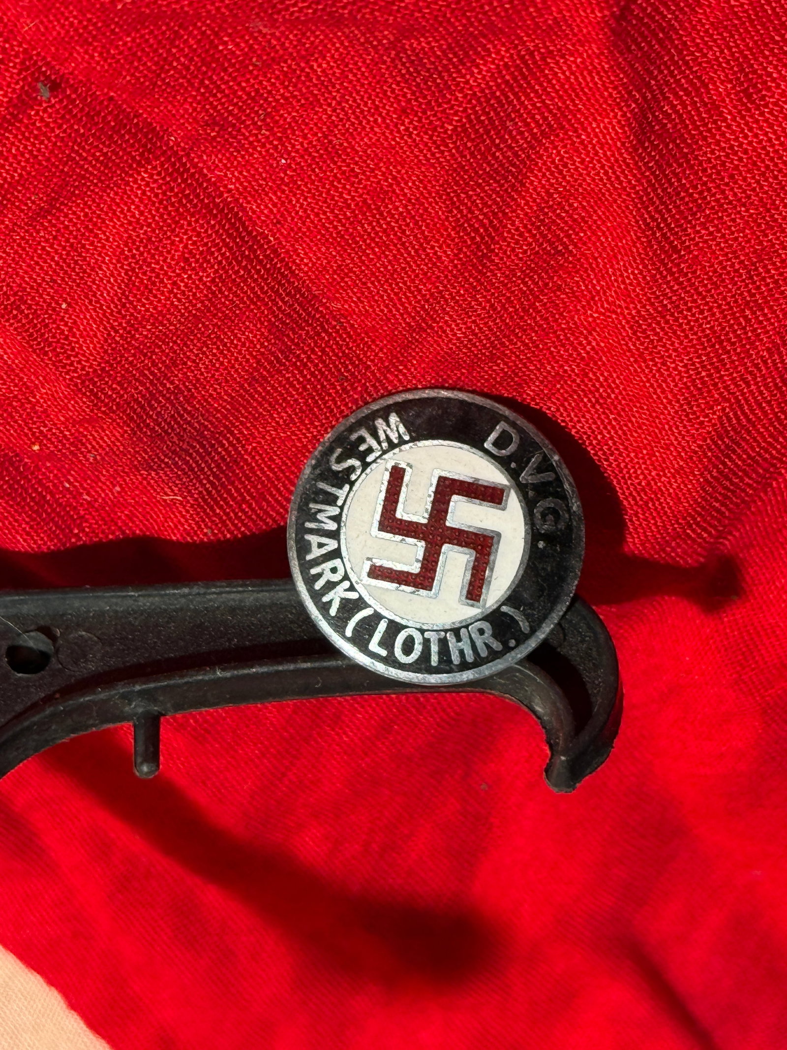 WW2 German D.V.G. Westmark (Lothringen) Political Badge By W. Redo: This circular enamel badge features a red swastika on a white background, surrounded by a black ring inscribed “D.V.G.” and “Westmark (Lothr.)”, referencing the German administrative r