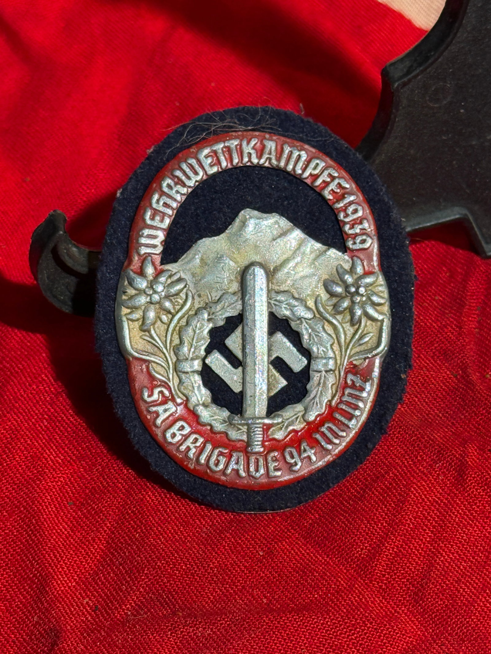 WW2 German SA “Wehrwettkämpfe 1939?? Badge – SA Brigade 94 (Munich) - Maker Marked: Commemorative badge issued for the 1939 SA Wehrwettkämpfe (paramilitary defense competitions). The design features Alpine imagery, edelweiss flowers, and a sword over a wreath enclosing a swastika, s