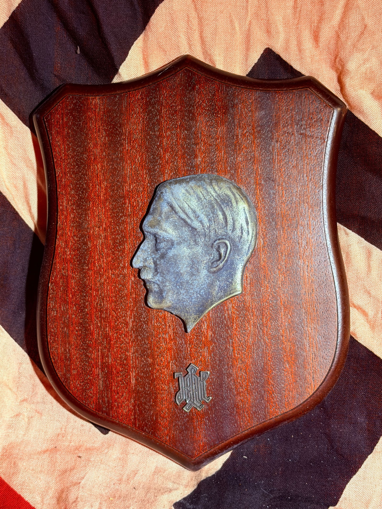 WW2 German Adolf Hitler Portrait Wall Plaque, Germany, c. 1930s–1945 With Eagle Stamp: Decorative wooden wall plaque featuring a metal relief profile portrait of Adolf Hitler, mounted on a shield-shaped stained wood backing. Beneath the portrait appears a stylized monogram emblem