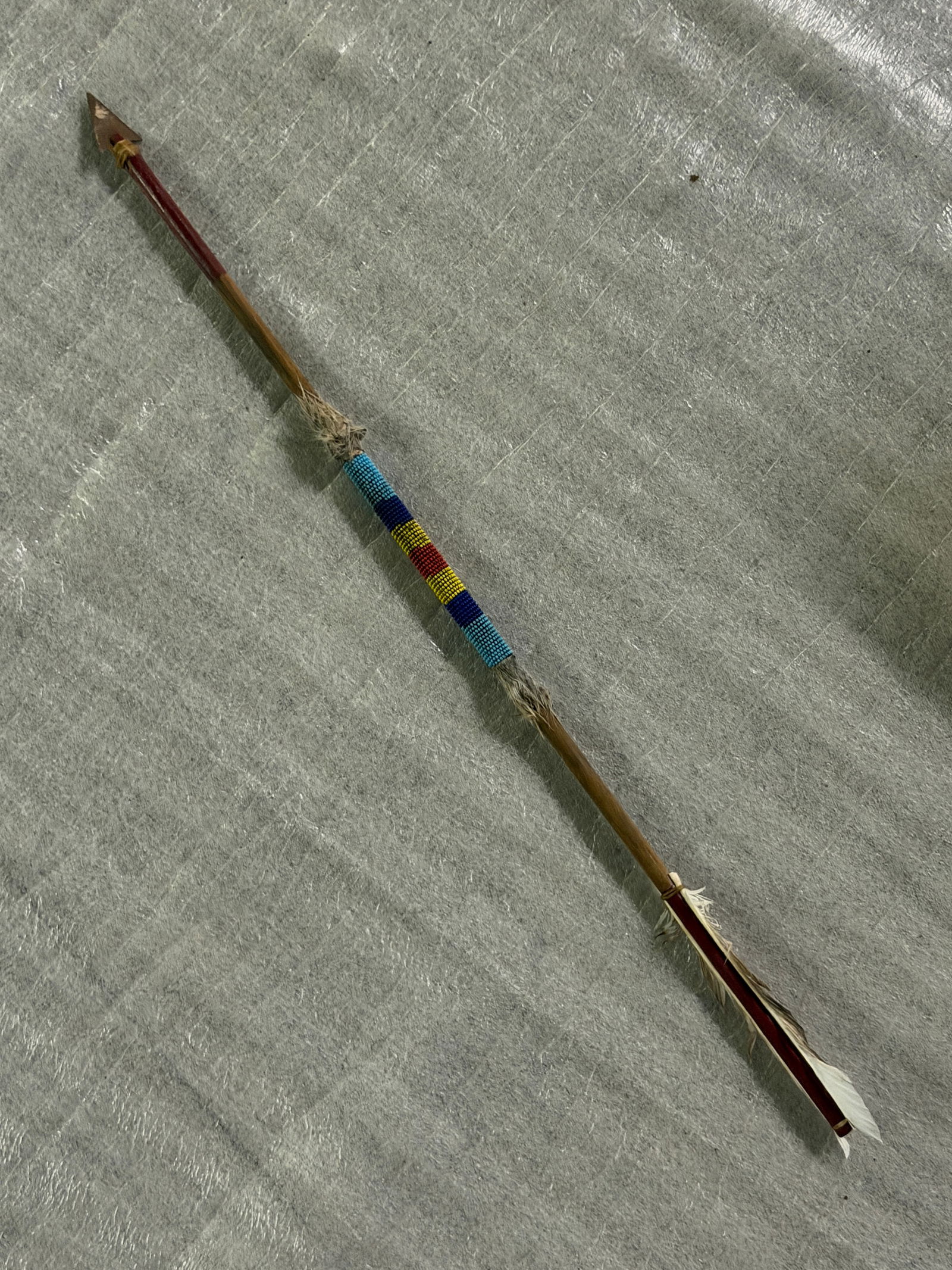 1800's Decorated Native American–Style Ceremonial Beaded Arrow: This handcrafted arrow features a wooden shaft fitted with a triangular metal arrowhead bound to the shaft with natural fiber cord. The midsection is decorated with a colorful band of glass beadwork i