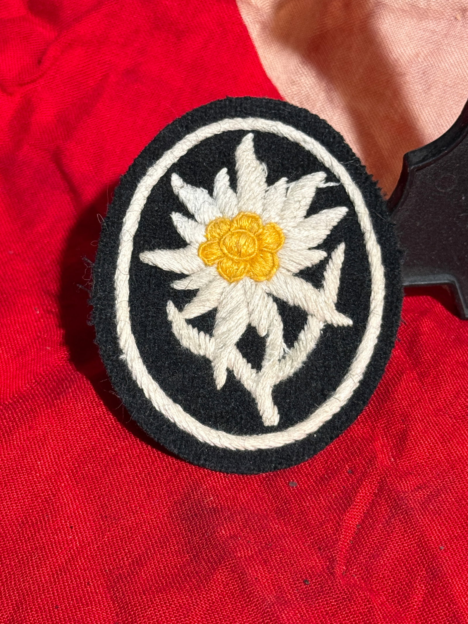 WW2 German Mountain Troops Edelweiss Sleeve Badge (Gebirgsjäger Insignia): This embroidered cloth badge features the Edelweiss flower, a symbol traditionally associated with alpine mountain troops. The white Edelweiss with a yellow center is stitched onto a black oval backin