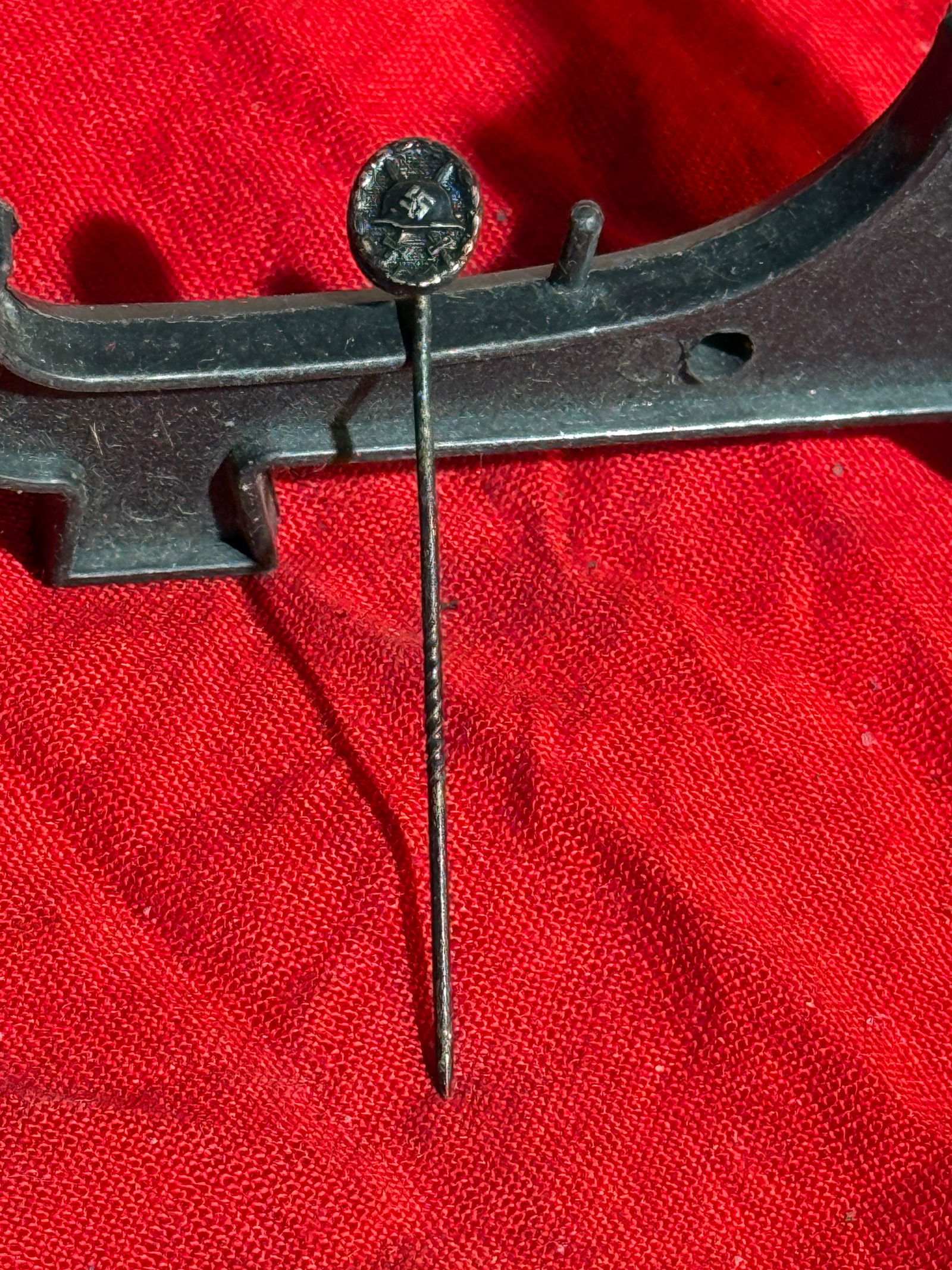 WW2 German Small Wound Badge Lapel Stick Pin – Third Reich Era: This small metal stick pin lapel badge dates to the Third Reich period (1933–1945). The circular head displays a swastika above crossed weapons, framed by a wreath motif, symbolizing military readin