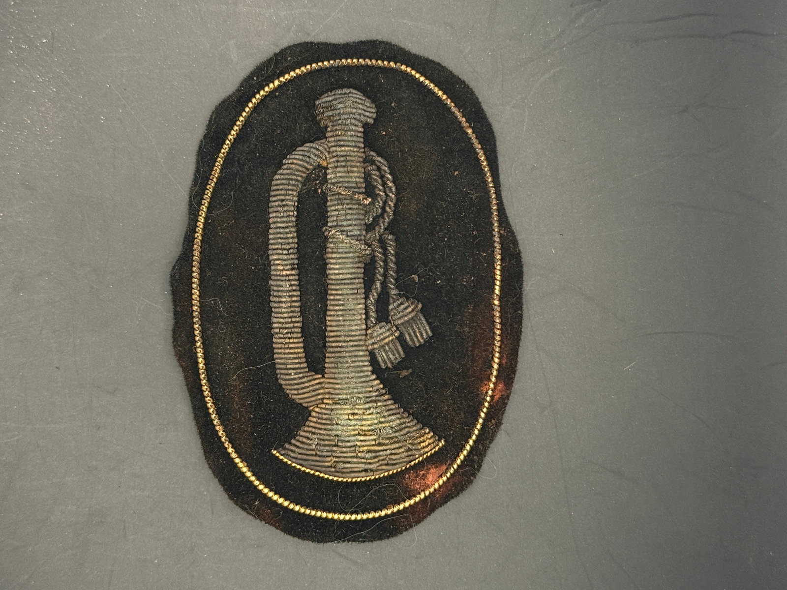 Civil War Rifleman Sharpshooter Bullion Headgear Badge by John A. Baker, New York: Civil War-era rifleman/sharpshooter headgear badge featuring a finely embroidered bugle horn in silver-gray bullion thread on a dark velvet or wool backing, bordered by a delicate gold bullion edge. T