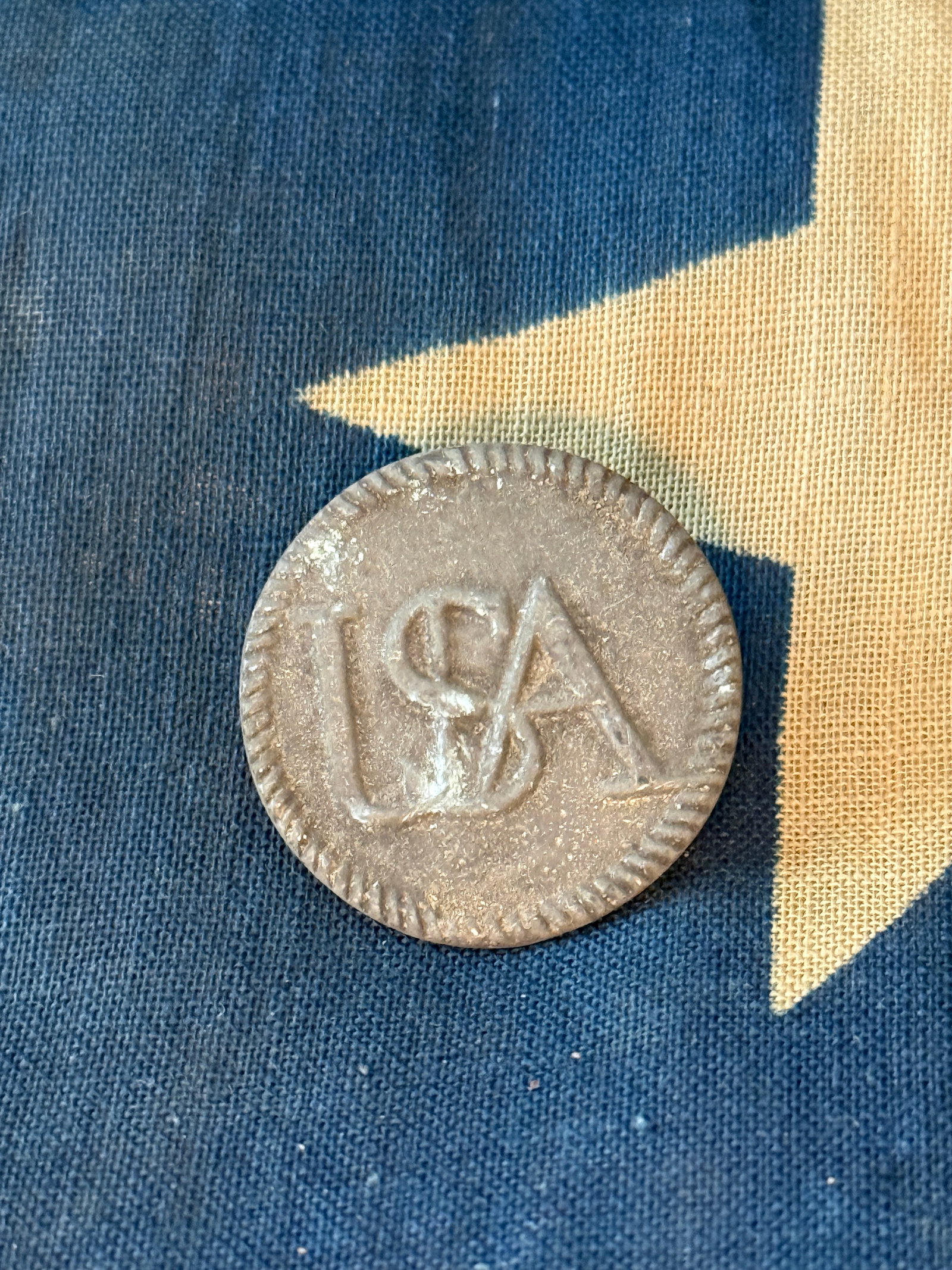American Revolutionary War USA monogram pewter button: Circular metal button featuring raised letters “USA” on the obverse within a decorative notched border. The reverse retains an integral loop shank for attachment to clothing. Buttons of this s