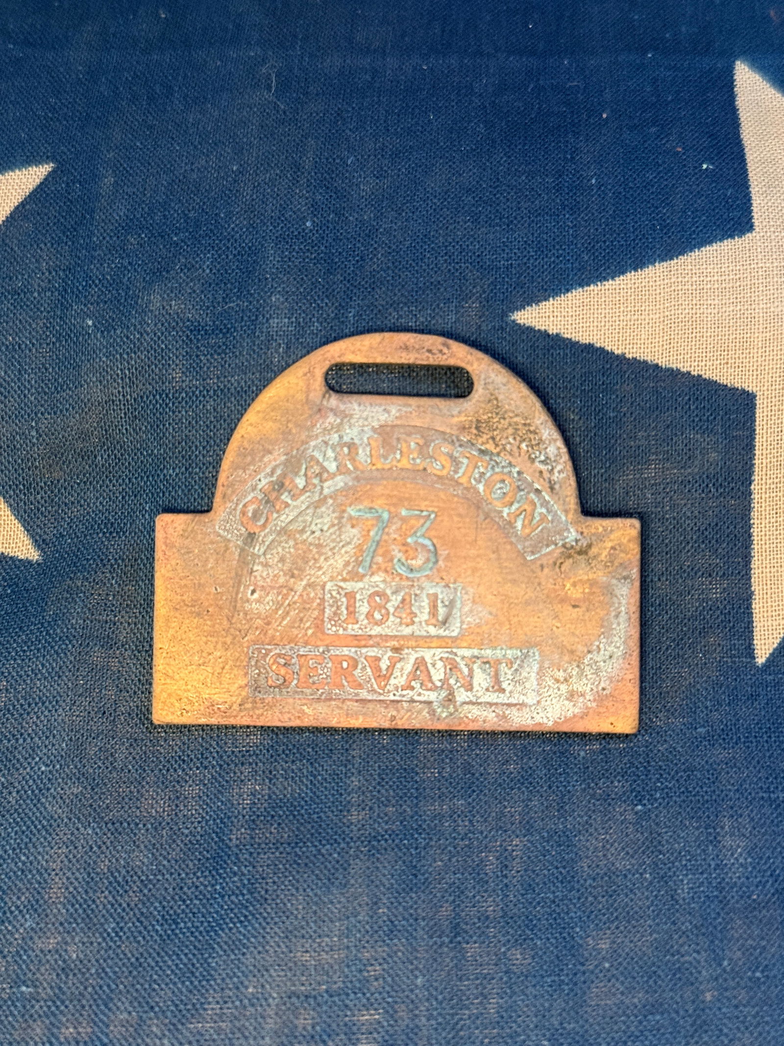 1841 Charleston Servant License Slave Tag Badge, No. 73: This brass identification badge was issued to a registered servant in Charleston, South Carolina, in 1841. The badge is stamped “CHARLESTON – 73 – 1841 – SERVANT,” indicating the license