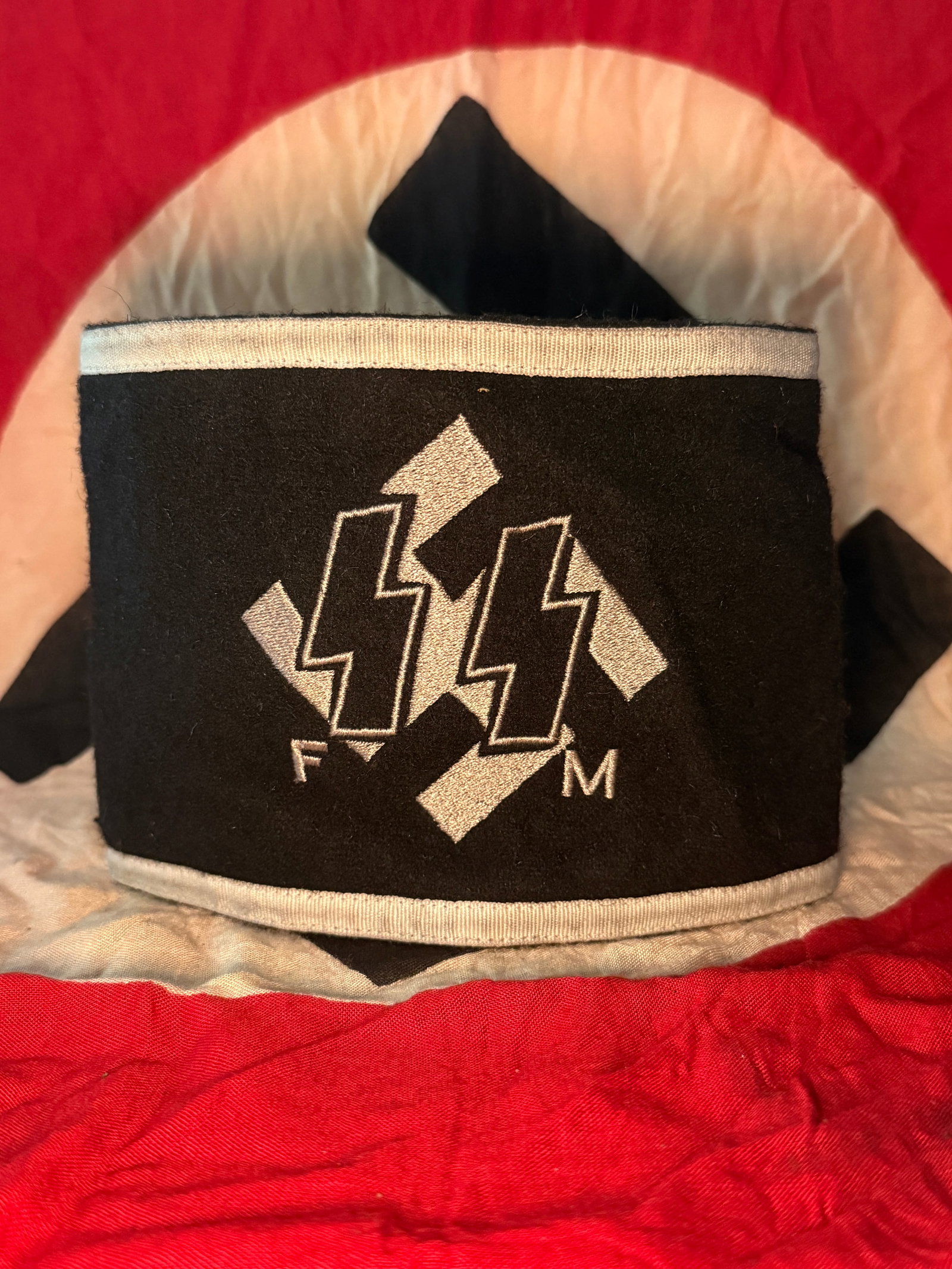 WW2 German SS Förderndes Mitglied (FM) Honorary Member armband: This black cloth armband bears the SS double “Sig” runes superimposed over a swastika, symbols associated with the Schutzstaffel (SS), the paramilitary organization of Nazi Germany. The letter