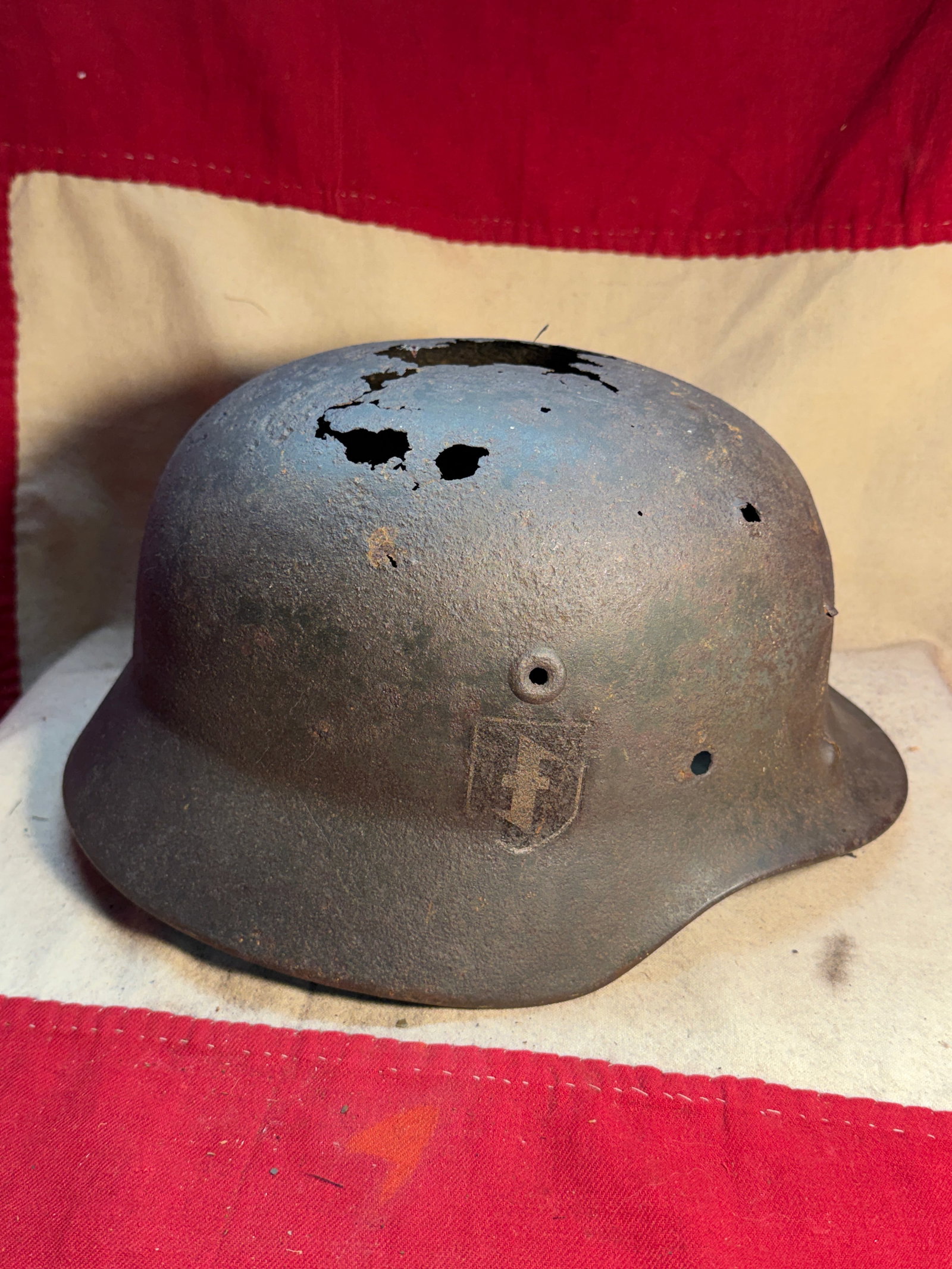 WW2 German M35 Steel Helmet (Stahlhelm) with Waffen-SS Decal, Battle-Damaged, c. 1935–1945: This German M35 steel helmet (Stahlhelm) represents one of the most recognizable pieces of military equipment used by German forces during the Second World War. Introduced in 1935, the M35 design feat