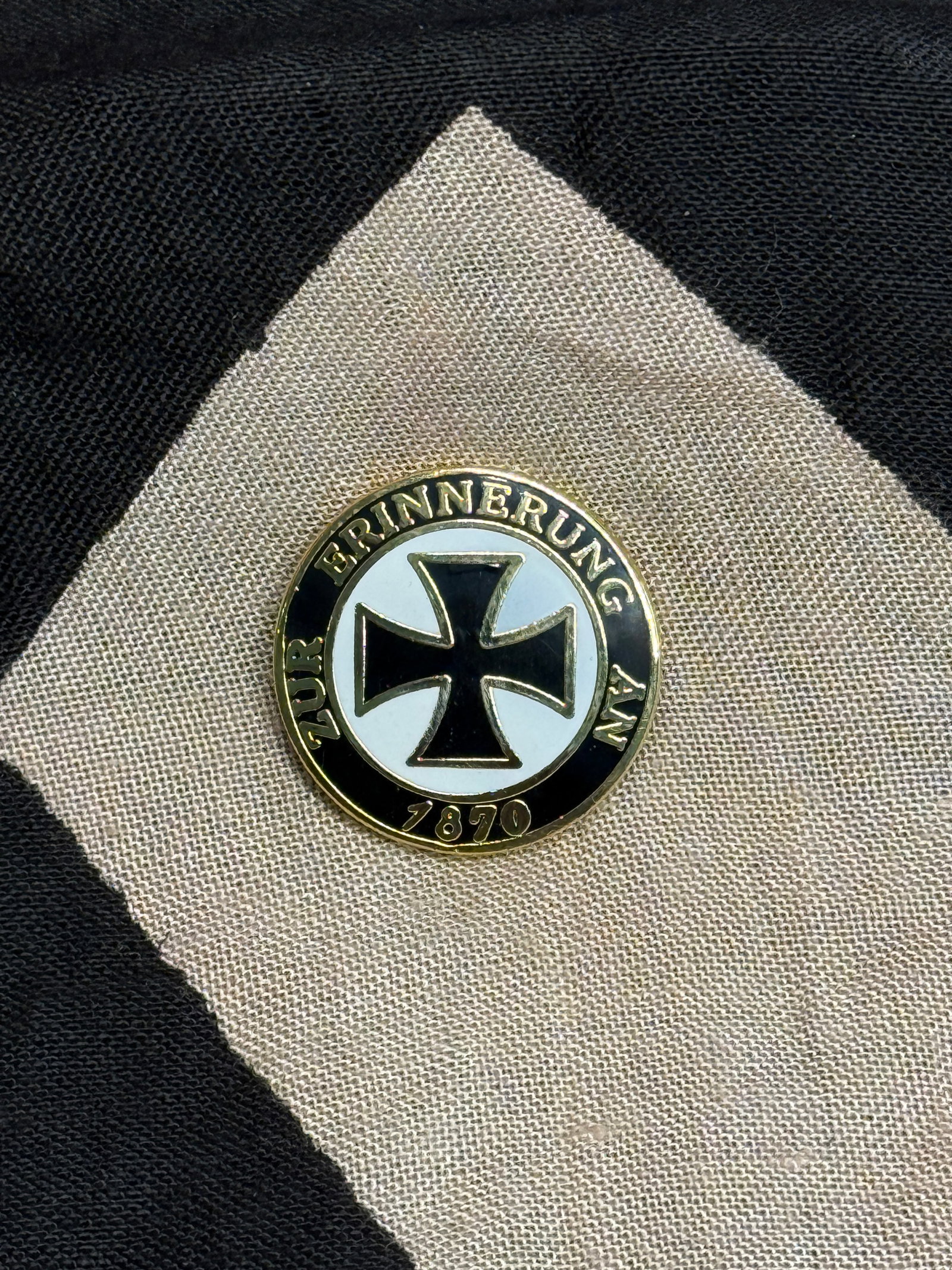 Commemorative Badge with Iron Cross Motif, “Zur Erinnerung an 1870: This circular metal badge features a black Iron Cross at its center, surrounded by the inscription “Zur Erinnerung an 1870” (“In memory of 1870”), referencing the Franco-Prussian War.