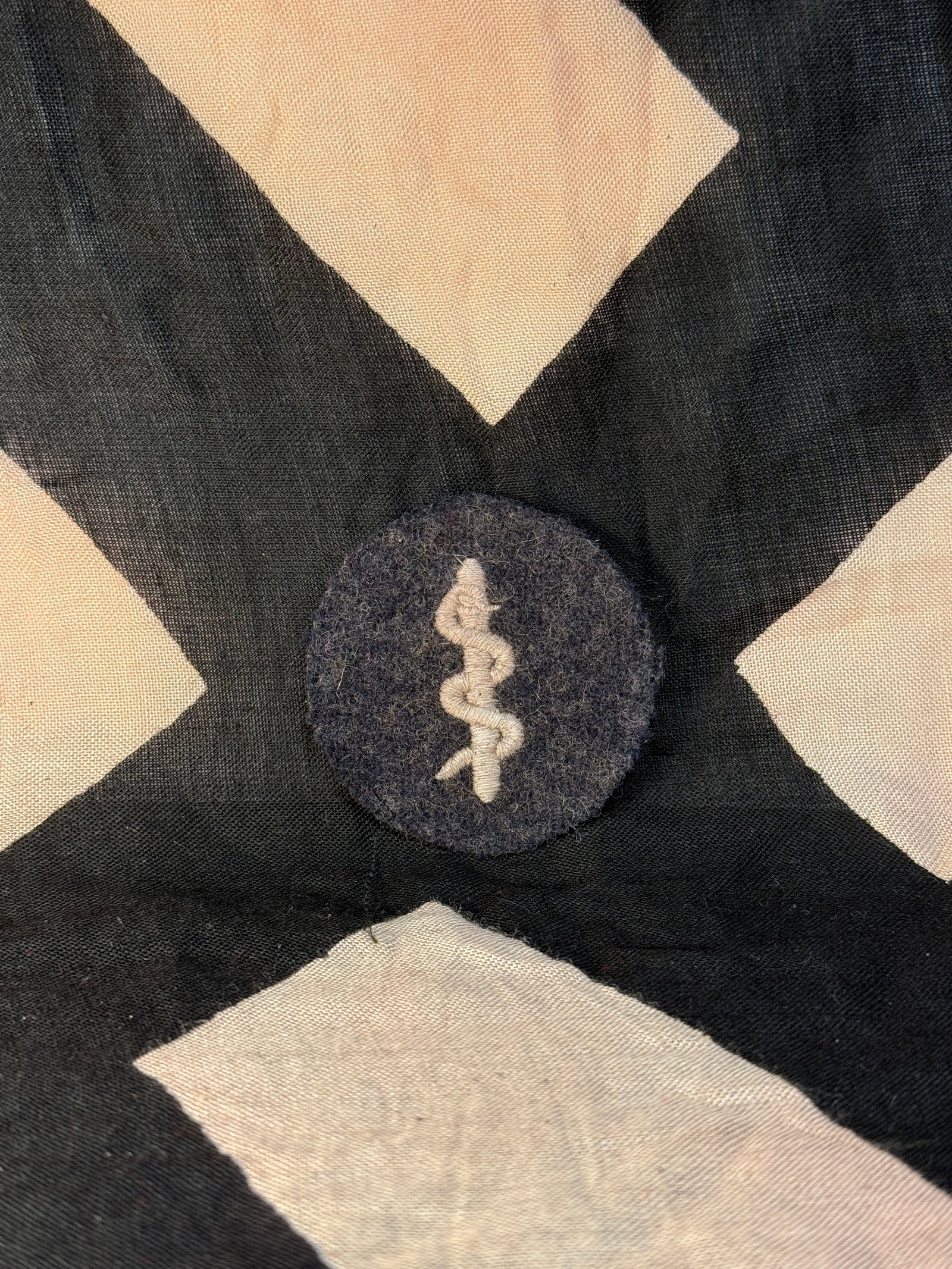 WW2 German Waffen-SS Medical Trade Badge (Sanitätsdienst Abzeichen): This circular dark-blue wool badge features a silver embroidered serpent entwined around a staff, a long-standing medical symbol. Worn on the uniform, it identified personnel serving in a medical or s