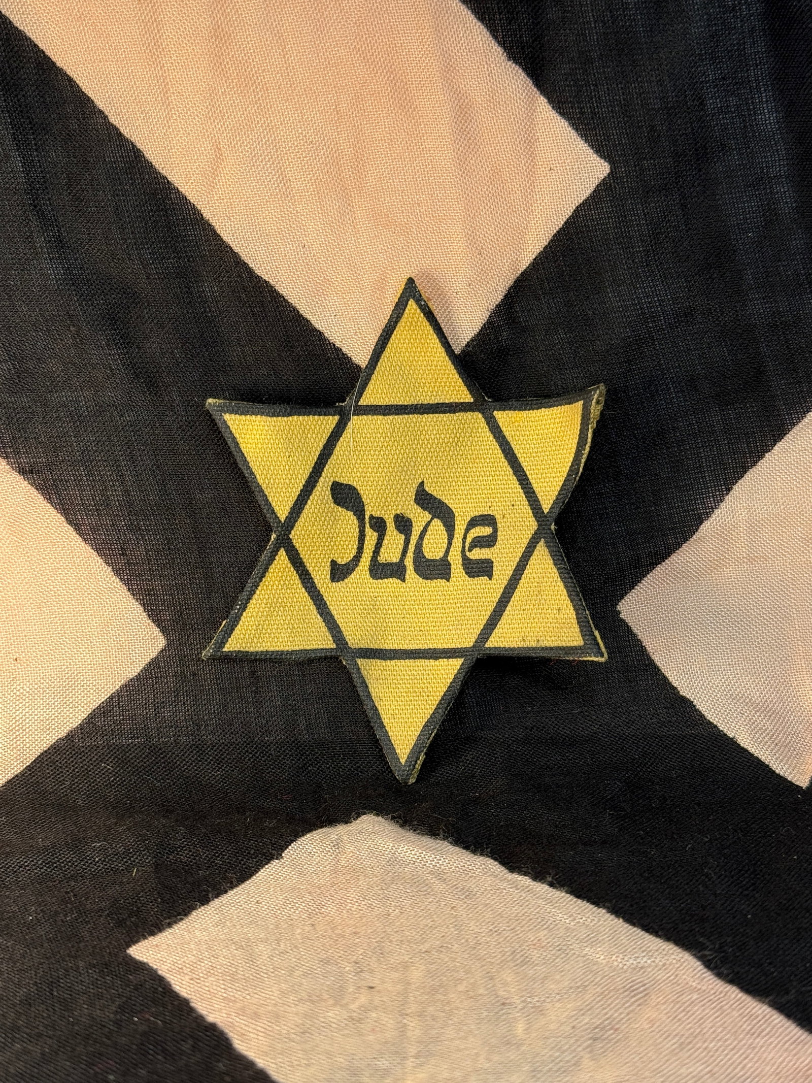 WW2 GERMAN Jewish Identity Star Of David Badge (“Judenstern??), Occupied Europe, c. 1941–1945: This yellow cloth Star of David bears the word “Jude” (“Jew”) in stylized black script. Such badges were forcibly worn by Jewish civilians under Nazi rule in occupied Europe as a means