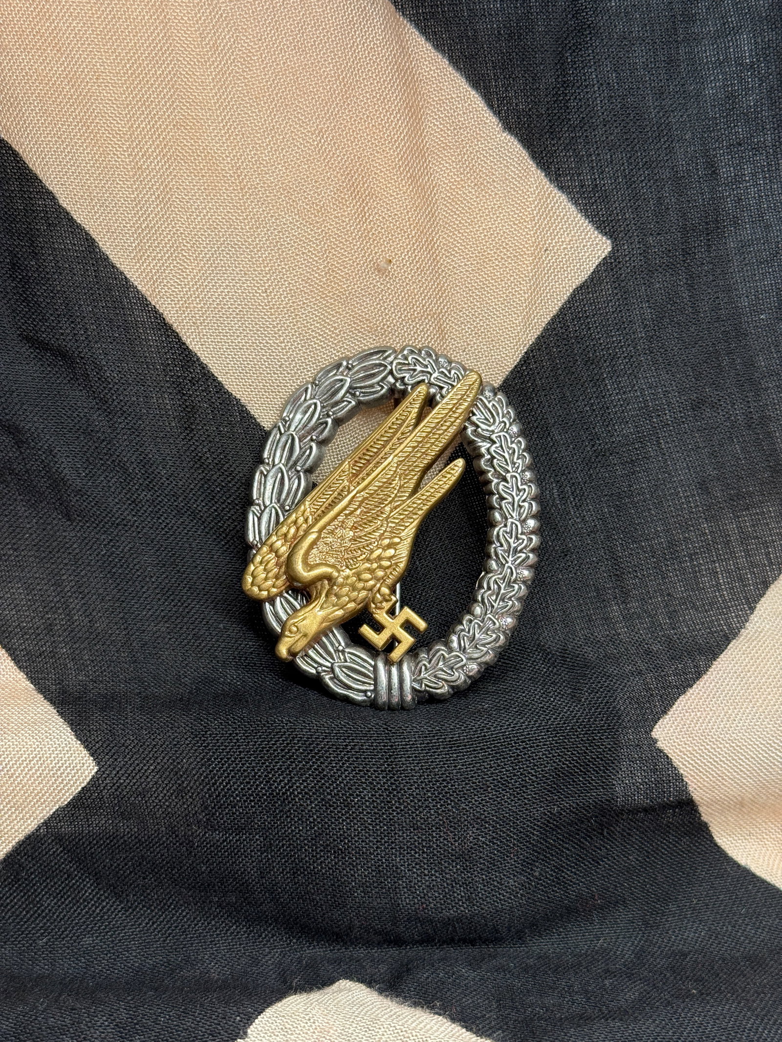 WW2 Fallschirmjäger Badge (Luftwaffe Paratrooper Qualification Badge), c. 1939–1945: This badge consists of a gilt diving eagle clutching a swastika, superimposed over a silvered wreath of laurel and oak leaves. Issued to qualified paratroopers of the German Luftwaffe, the Fallschirmj