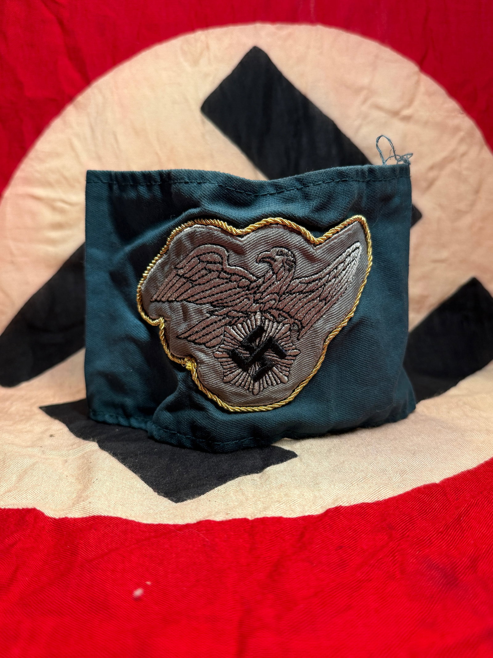 WW2 German Luftschutz Armband with National Eagle, Germany, c. 1939–1945: This blue-green cloth armband bears a machine-embroidered national eagle clutching a wreath with swastika, set on a shaped backing and bordered with gold-colored cord. The coloration and construction