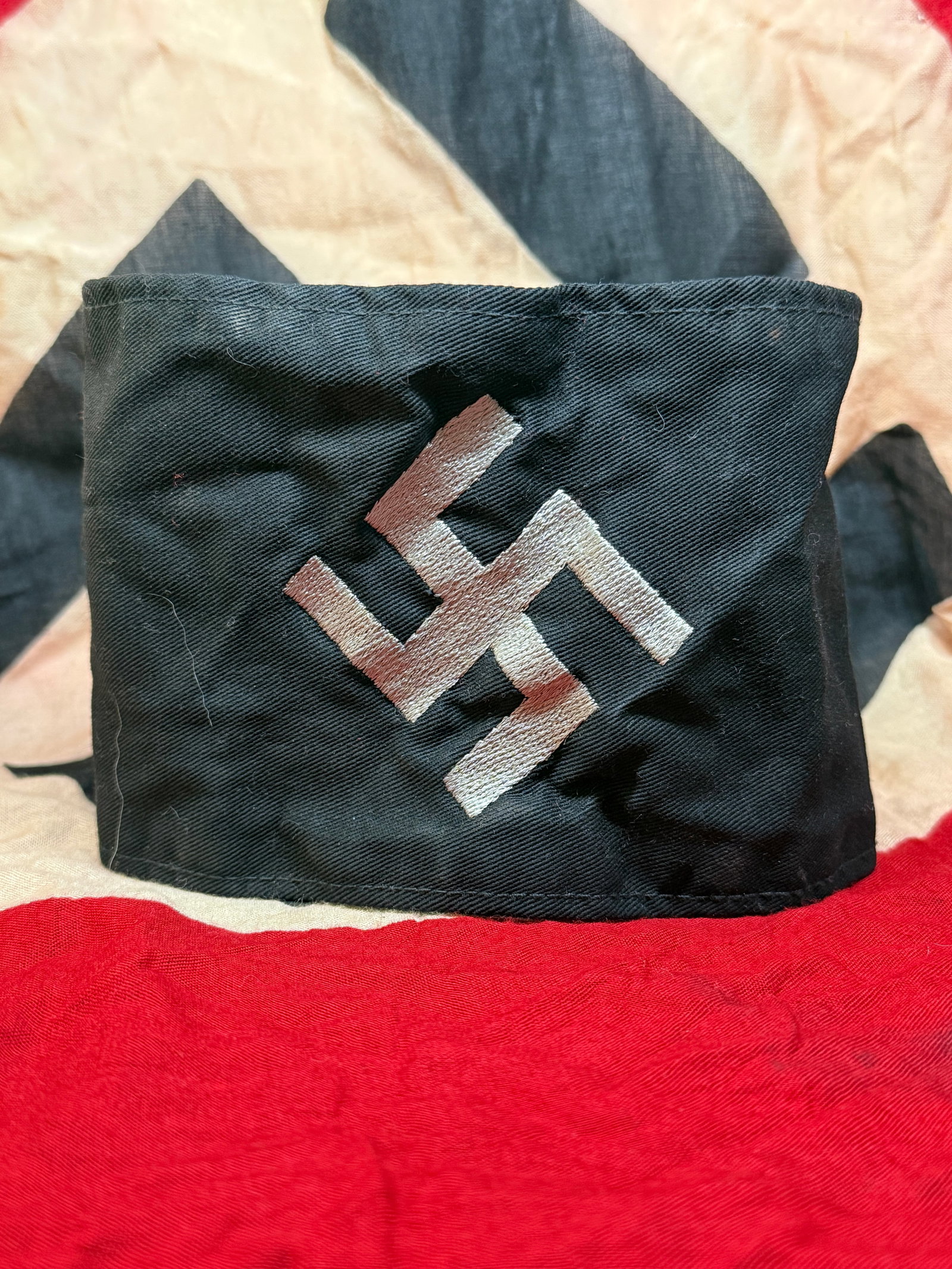 WWII GERMAN HITLER YOUTH ARMBAND: This black fabric armband features a swastika symbol rendered in a contrasting light-colored material. The swastika, historically an ancient symbol found in many cultures, was appropriated by the Nati