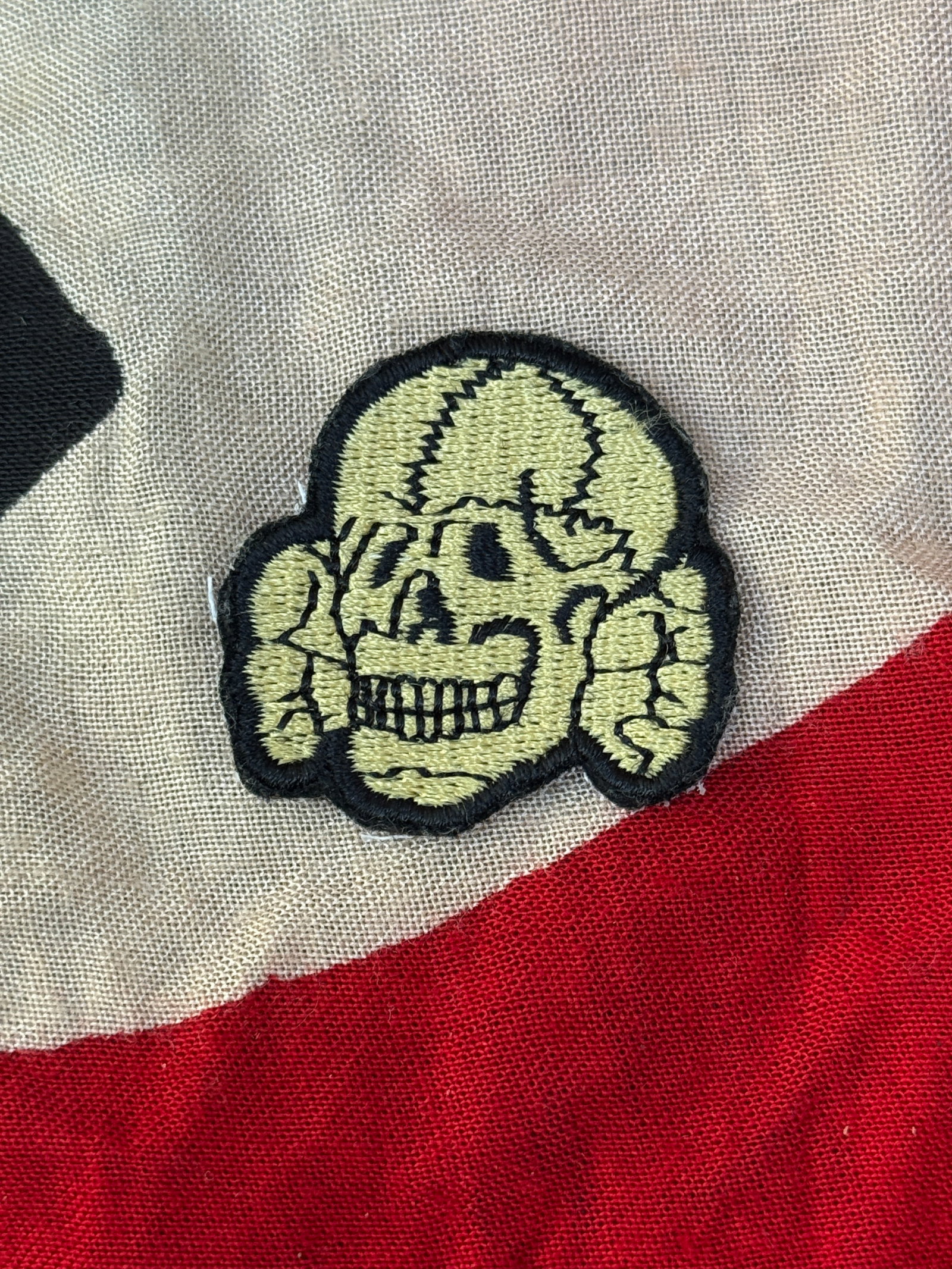 WWII German Waffen-SS Totenkopf (Skull) Uniform Insignia: This embroidered cloth insignia depicts the “Totenkopf” (death’s head), a skull motif historically associated with German military units and most notably used by the Waffen-SS during the Sec