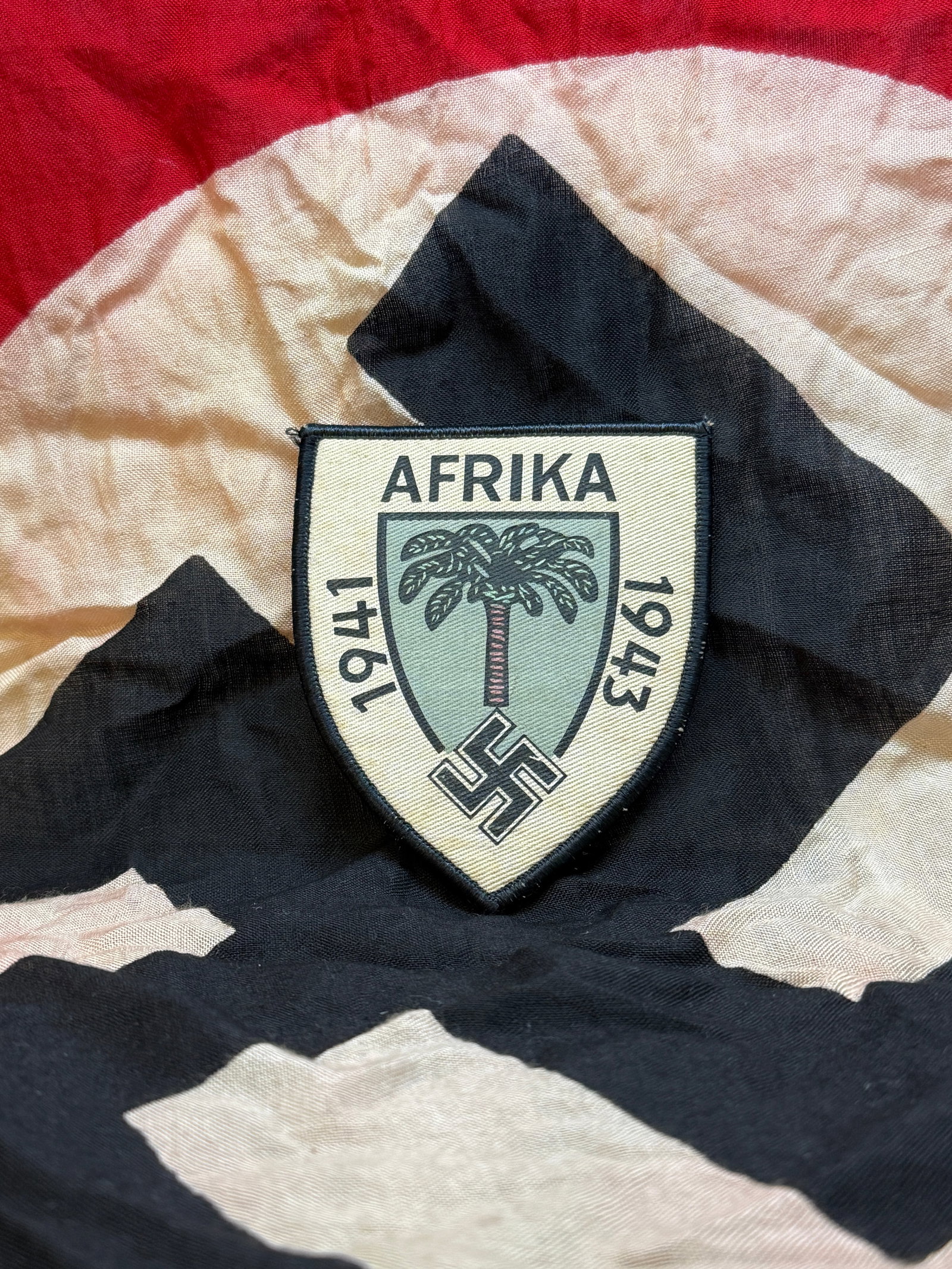 Afrika Corps Insignia Patch (World War II, 1941–1943): This cloth insignia patch is associated with the German Afrika Korps, a military force deployed by Nazi Germany during World War II in North Africa. The design features a palm tree—symbolizing the d