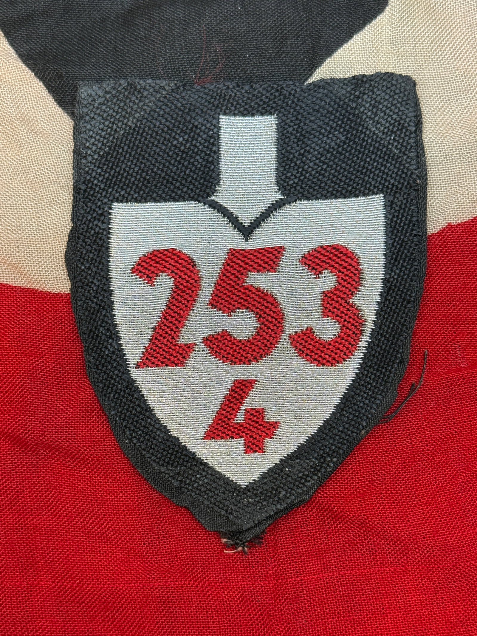 WWII German Medical/Unit Identification Cloth Patch (“253/4??): This embroidered shield displays red numerals “253” above a smaller “4,” possibly denoting a unit, company, or medical formation. The white shield and cross-like upper form suggest a c