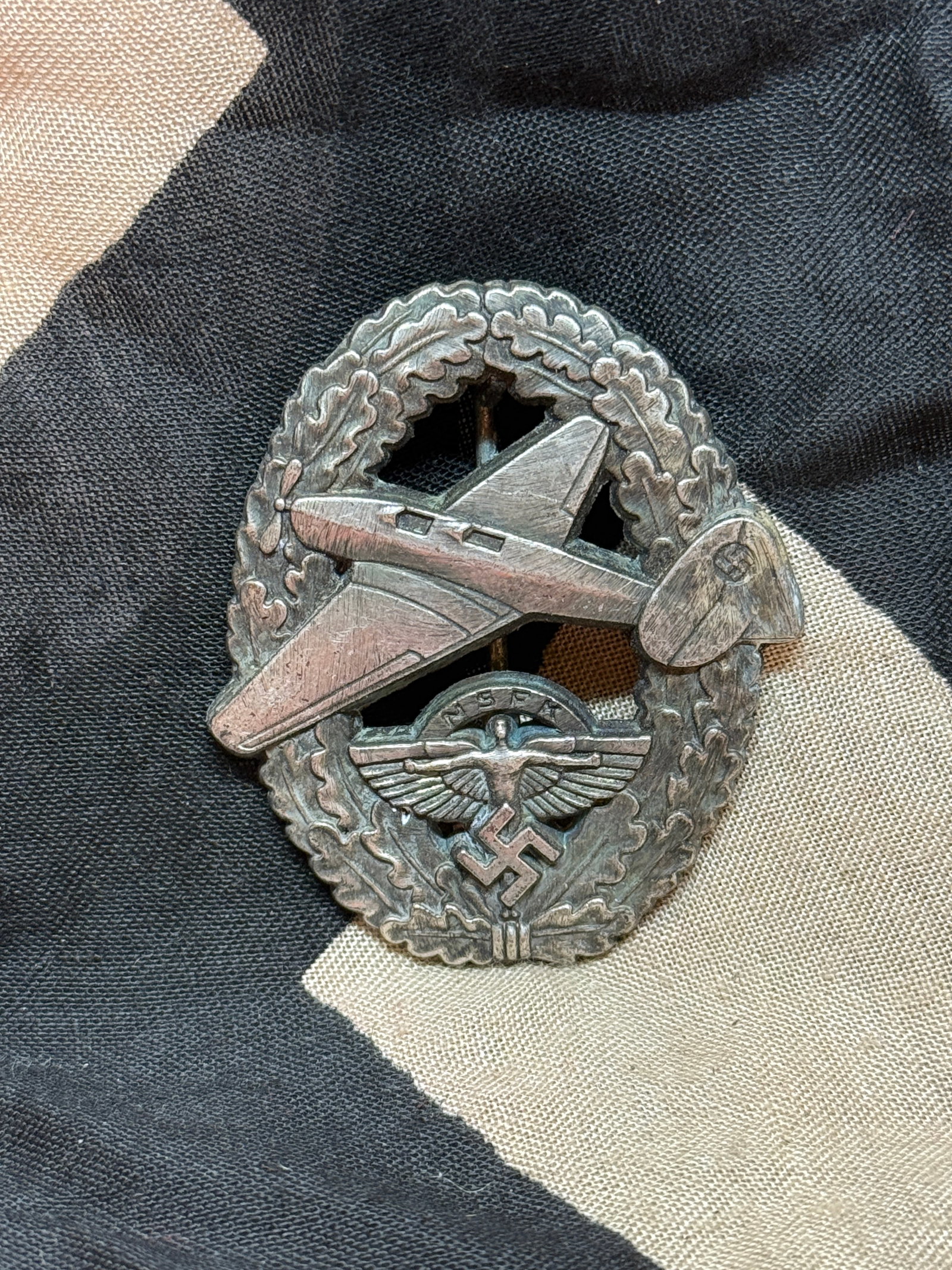 World War II German NSFK Glider Pilot Badge (National Socialist Flyers Corps): A metal badge depicting a glider aircraft superimposed over a wreath, with the NSFK eagle and swastika emblem beneath. Awarded to members of the National Socialist Flyers Corps (NSFK), this badge reco