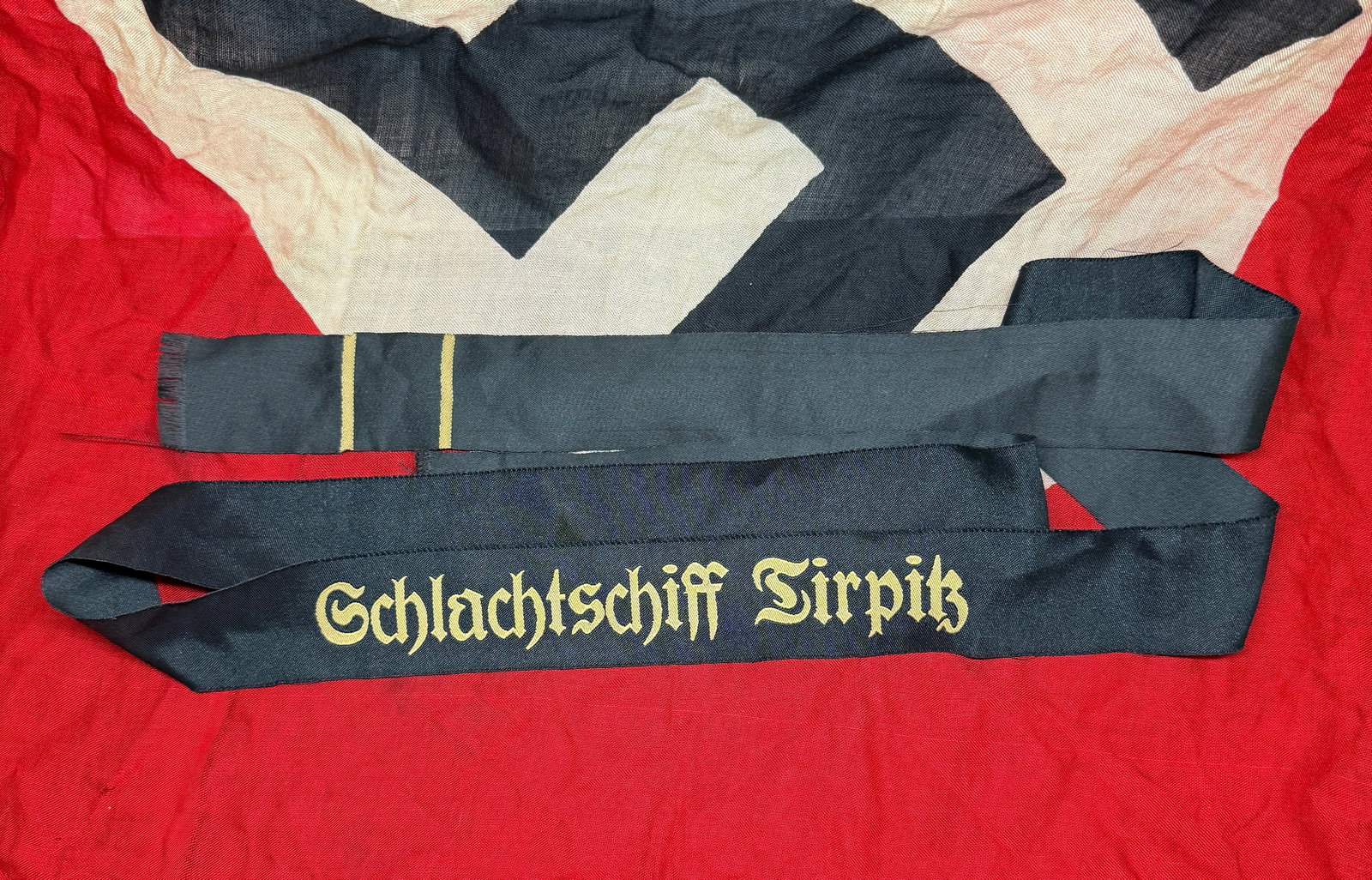 WW2 German Kriegsmarine Cap Tally – “Schlachtschiff Tirpitz,?? c. 1939–1945: This black silk cap tally (Mützenband) bears the gilt-embroidered inscription “Schlachtschiff Tirpitz,” identifying it with the German battleship Tirpitz, one of the largest and most powerful
