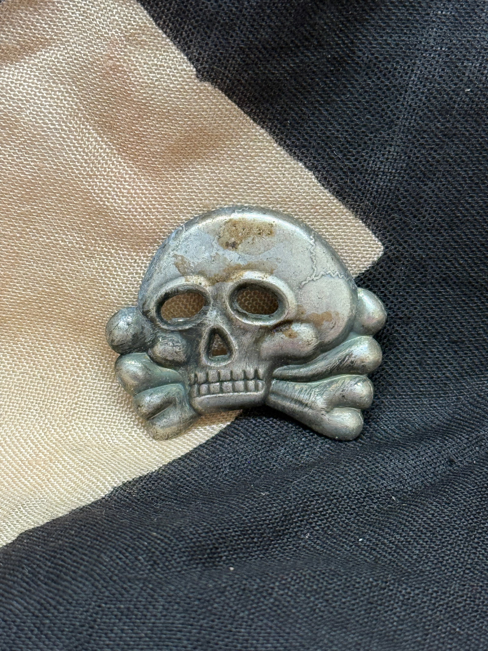 WWII German SS Skull (Totenkopf) Cap Insignia: This metal skull and crossbones badge, known as the Totenkopf, was worn on the caps of SS personnel during World War II. The design, featuring a stylized human skull above crossed bones, symbolized lo