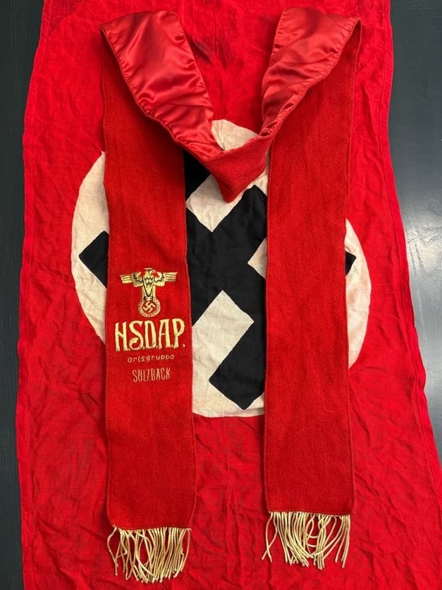 WWII German NSDAP Ortsgruppe Ceremonial Sash (Sulzbach): This red ceremonial sash is embroidered with the insignia of the National Socialist German Workers’ Party (NSDAP), including a stylized eagle clutching a wreath and swastika above the inscription ��